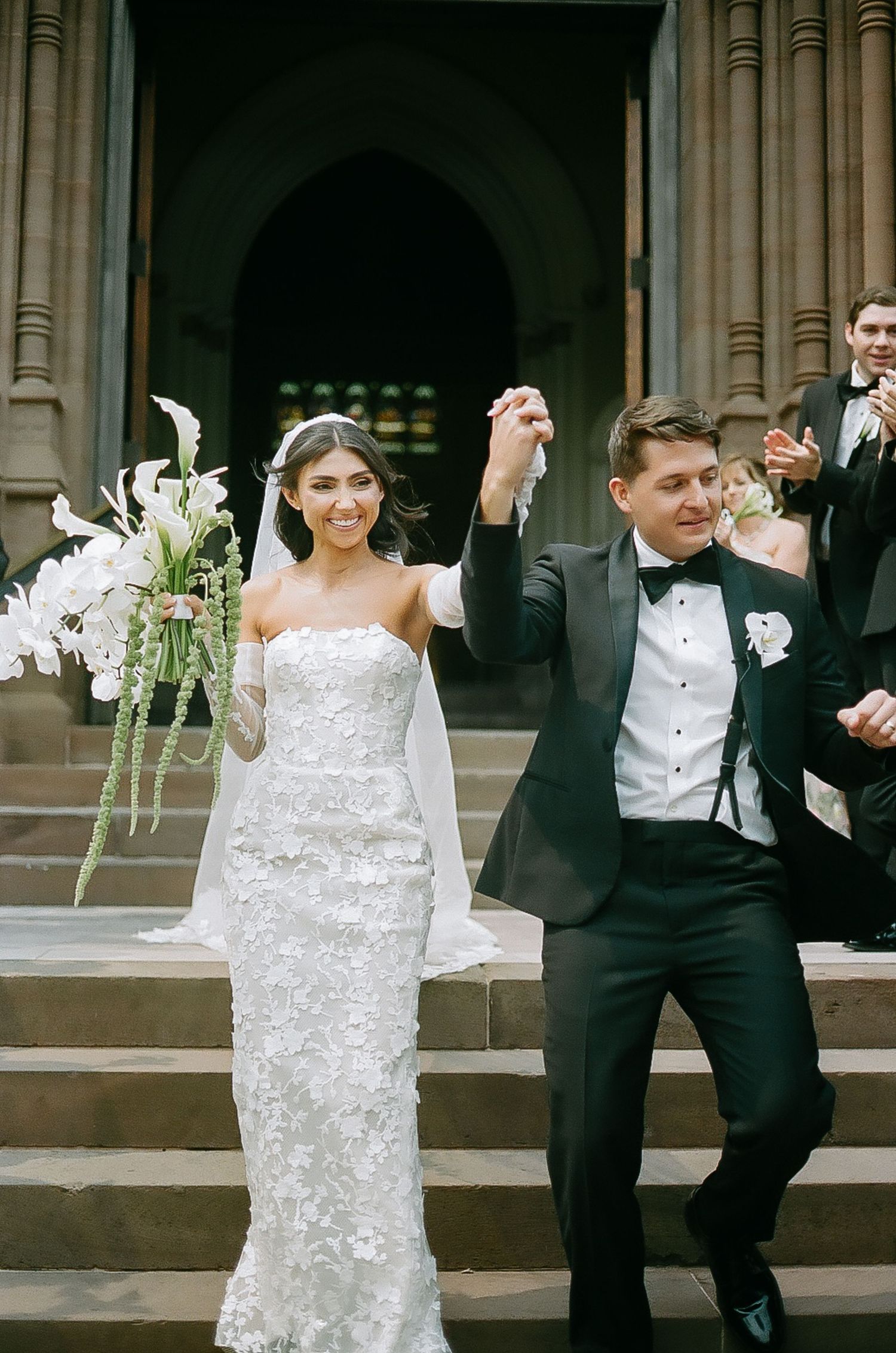 Newlyweds dance and celebrate with joyful movements on outdoor stone steps.