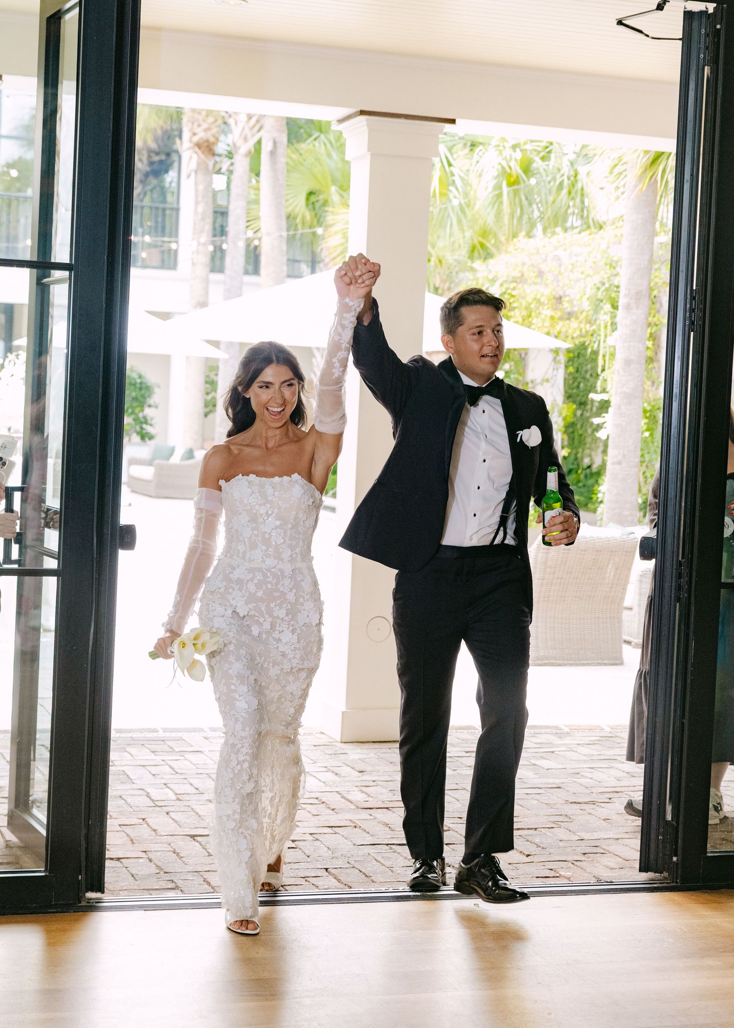 Wedding party makes grand entrance through glass doors at venue reception.