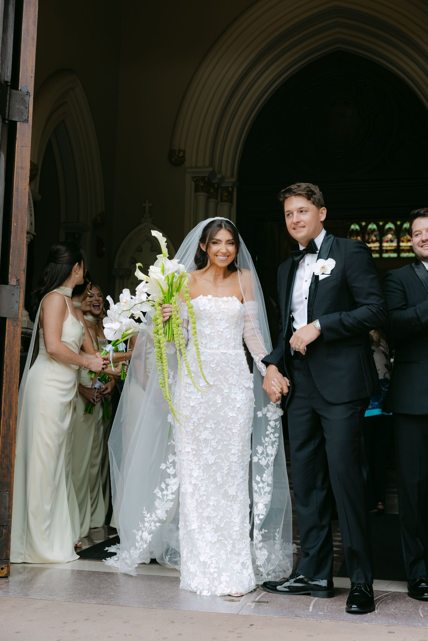Bridal party poses under arched church doorway with white and green floral bouquets.