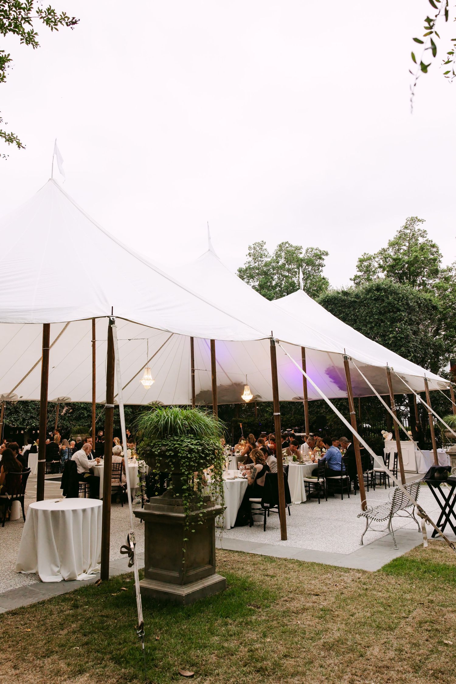 Outdoor wedding reception under a white sailcloth tent at dusk with guests dining and purple ambient lighting.