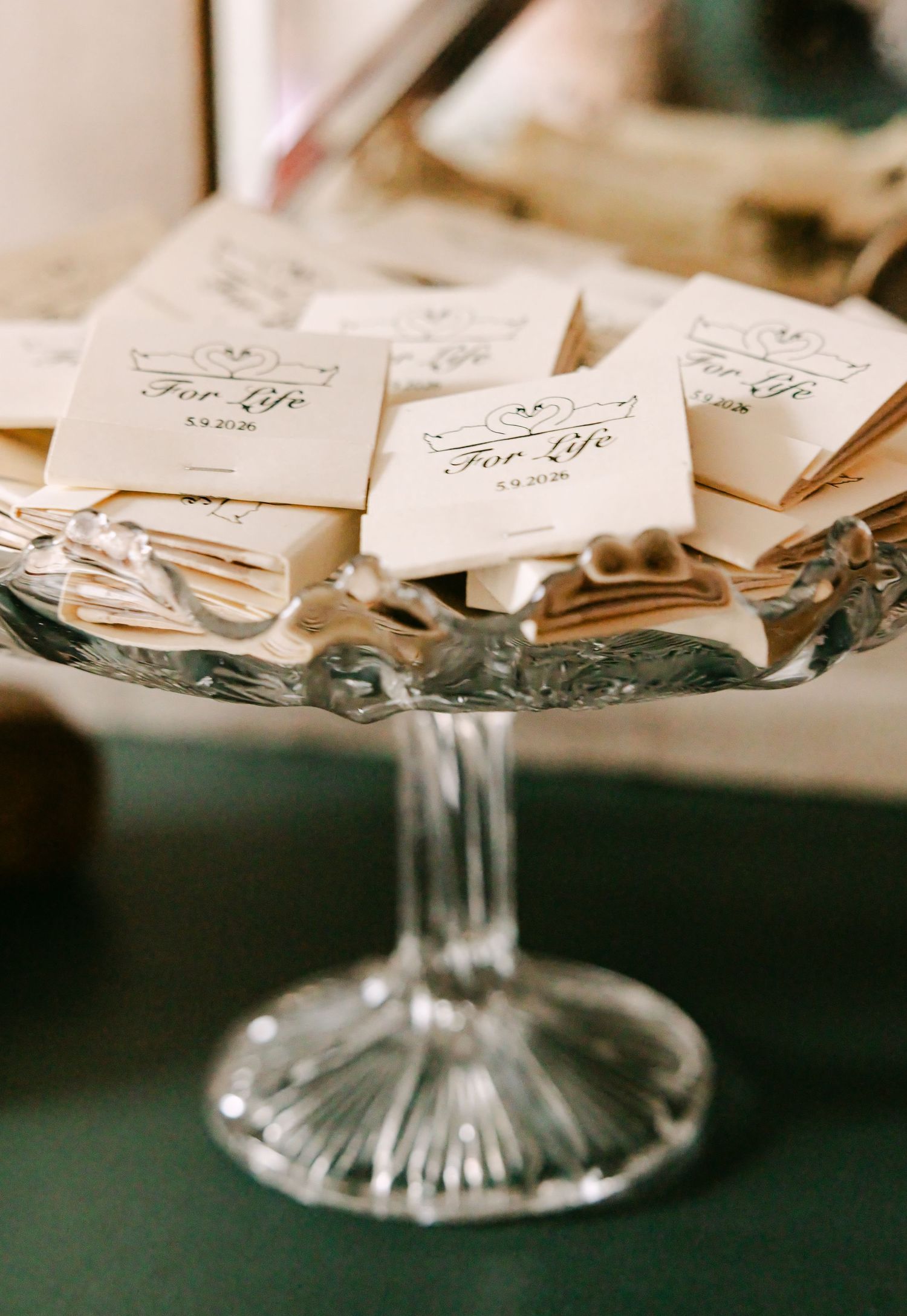 Crystal pedestal dish displaying elegant wedding favor packets inscribed with For Life and a date.