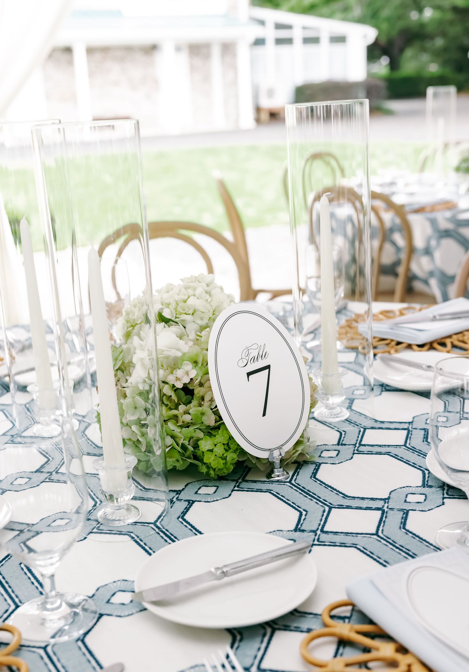Elegant wedding reception table with blue geometric linen, white hydrangea centerpiece, and oval table number seven card.