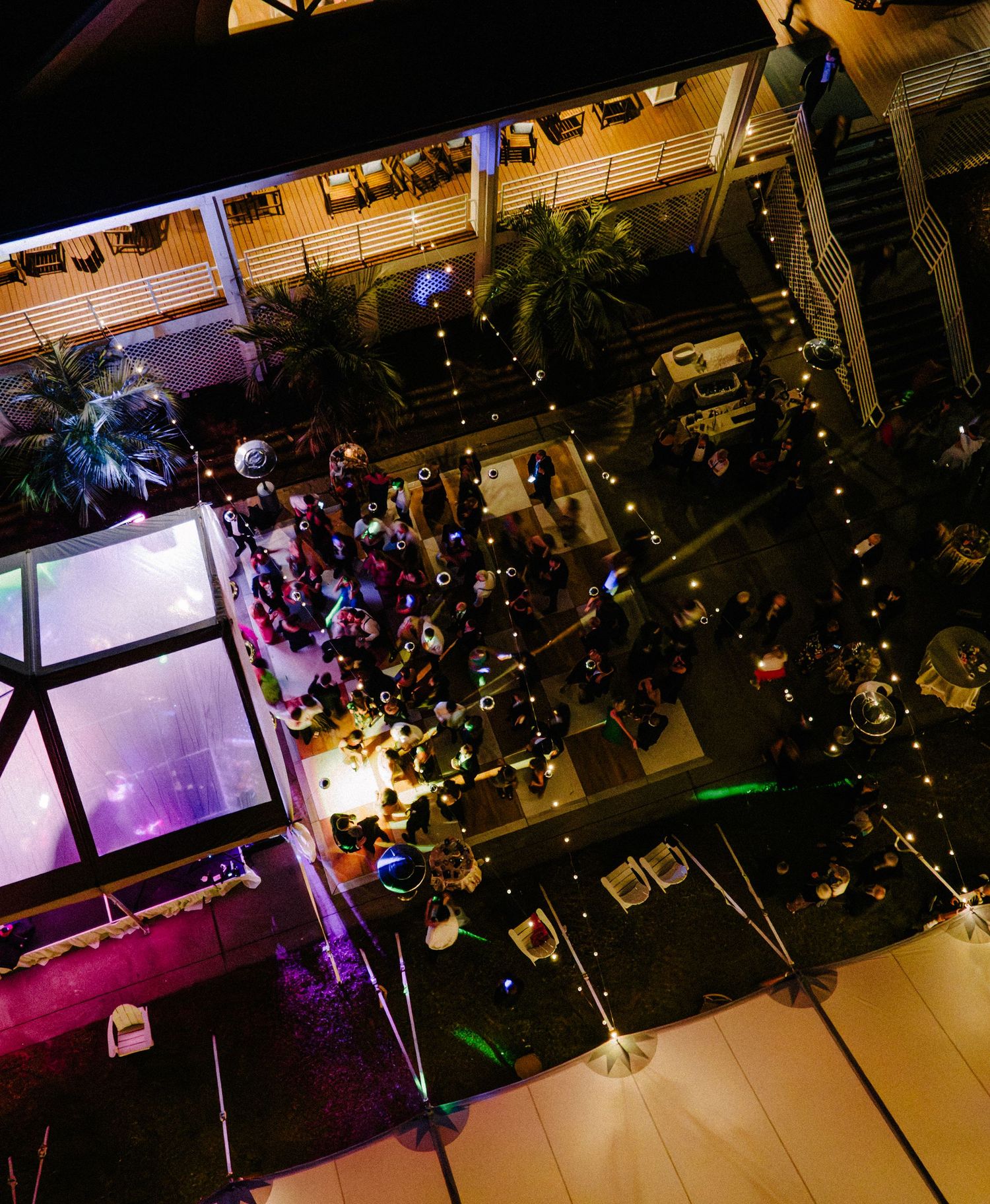 Aerial night view of lively outdoor wedding reception with dance floor and string lights.