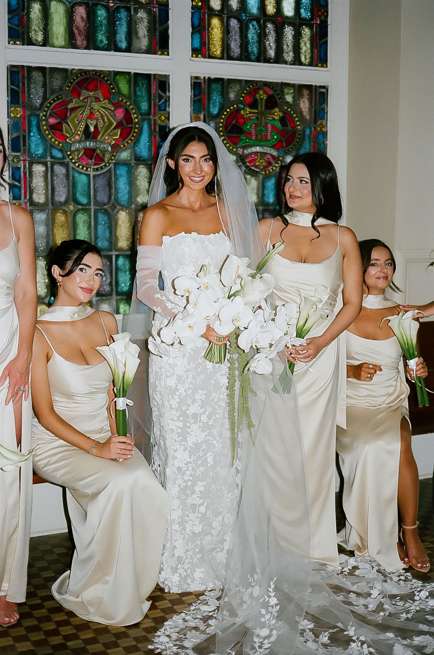 Bridal party poses together in white dresses against a backdrop of colorful vintage bottles.