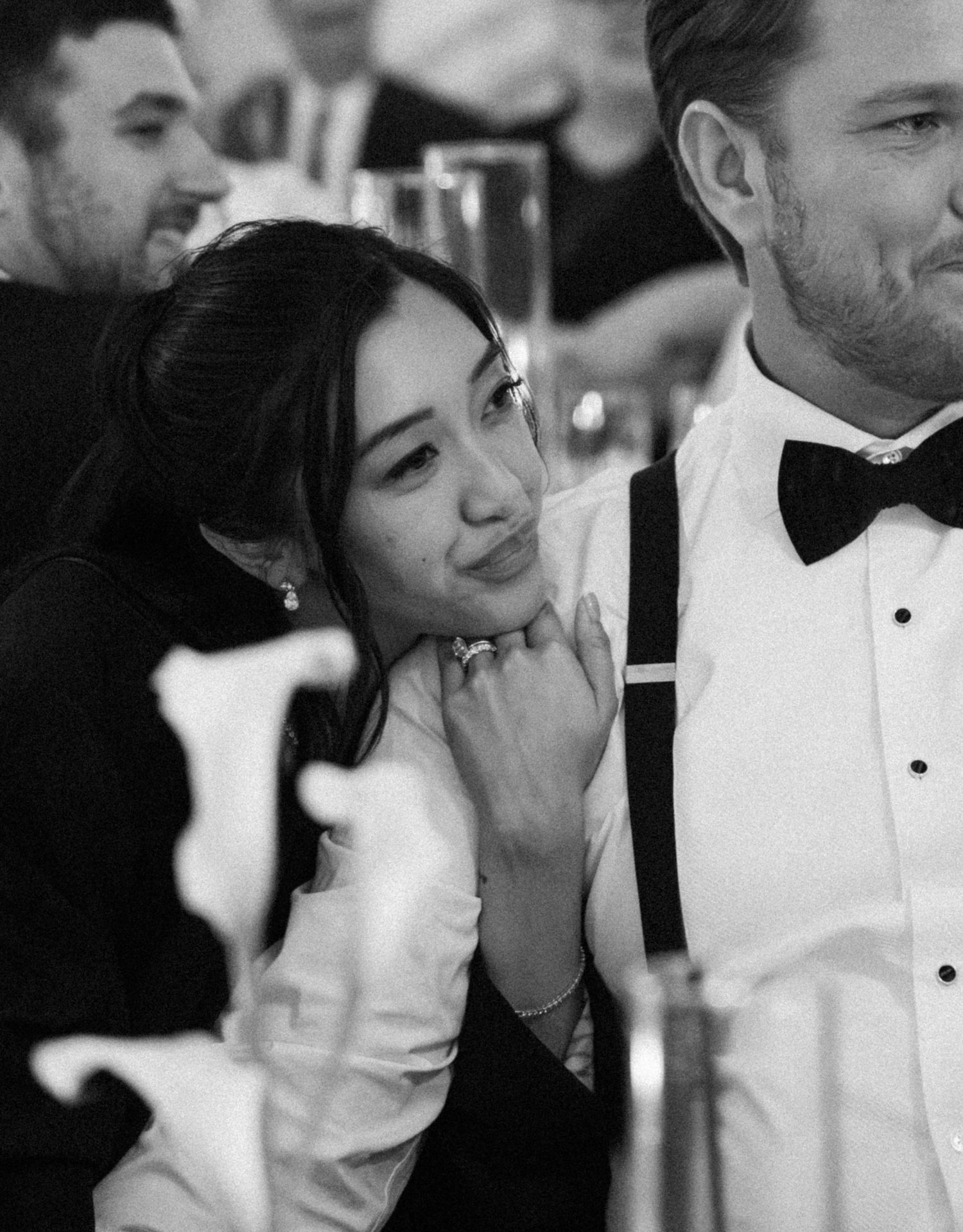 Emotional wedding guest in white shirt leaning thoughtfully during indoor reception in black and white photo.