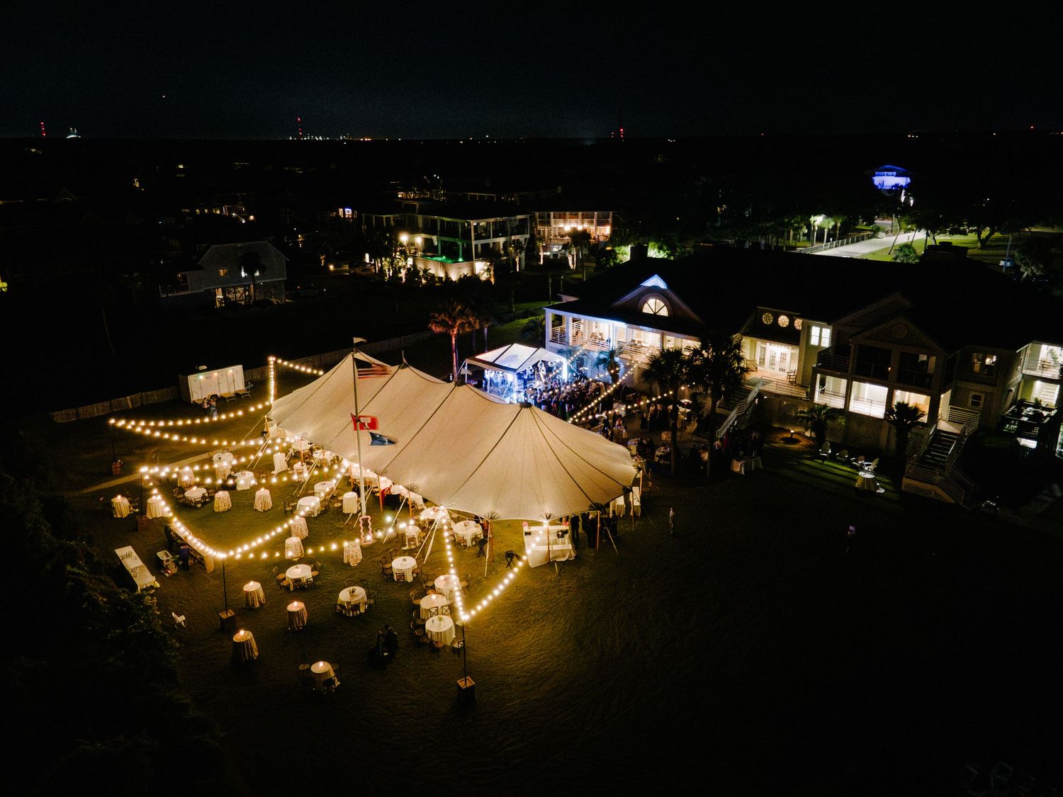 Aerial night view of elegant outdoor wedding venue with sailcloth tent and string lights.