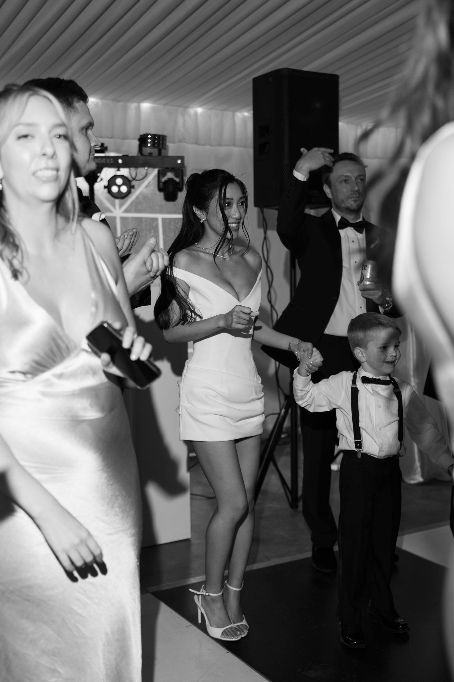 Bride in white mini dress dancing with guests on checkered floor at wedding reception.