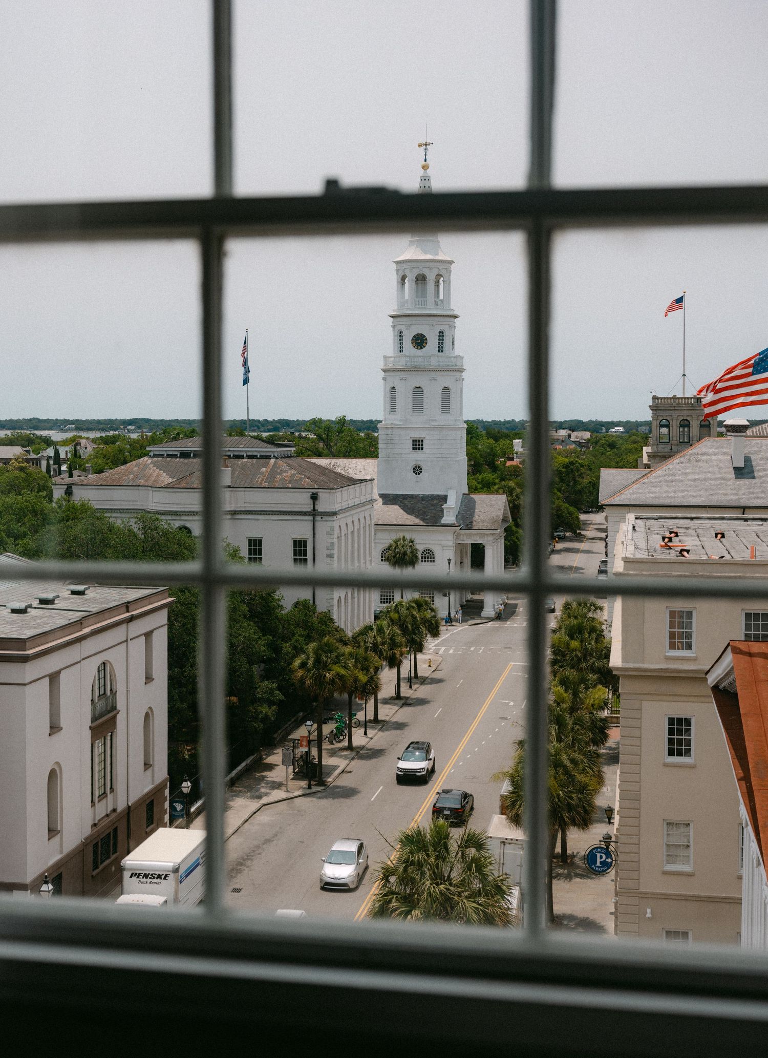 Historic church steeple with American flag viewed through window in Charleston.