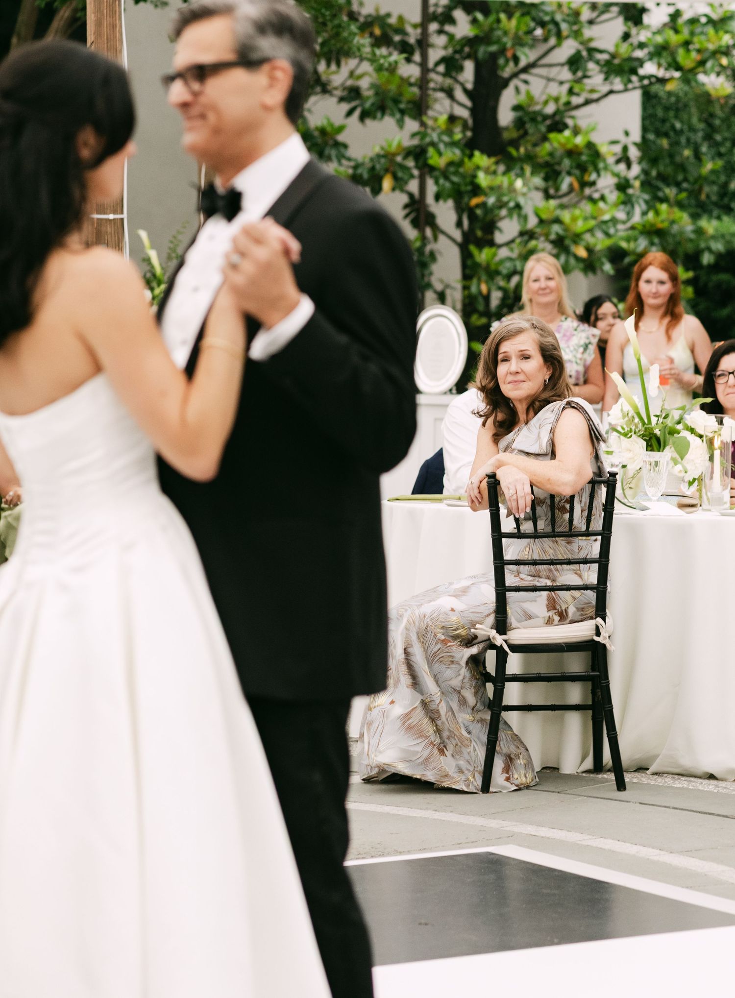 Bride and groom share first dance while wedding guests watch with joy at outdoor reception.