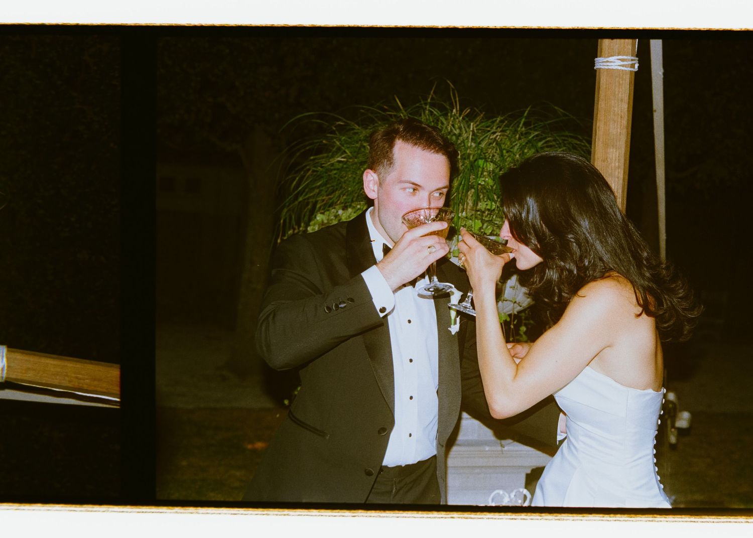 Bride and groom sharing a toast together during outdoor wedding reception at night.
