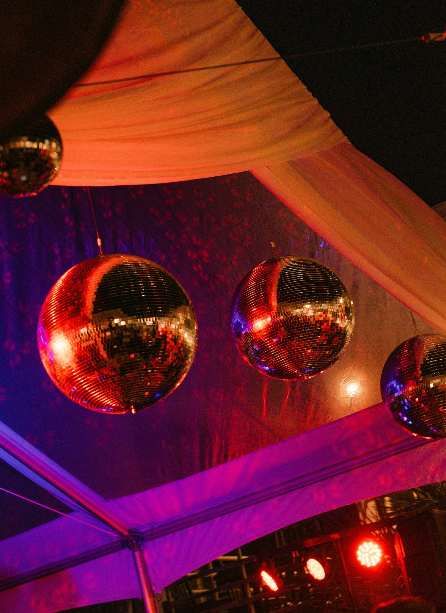 Glittering disco balls hanging under draped tent ceiling with purple and orange lighting.
