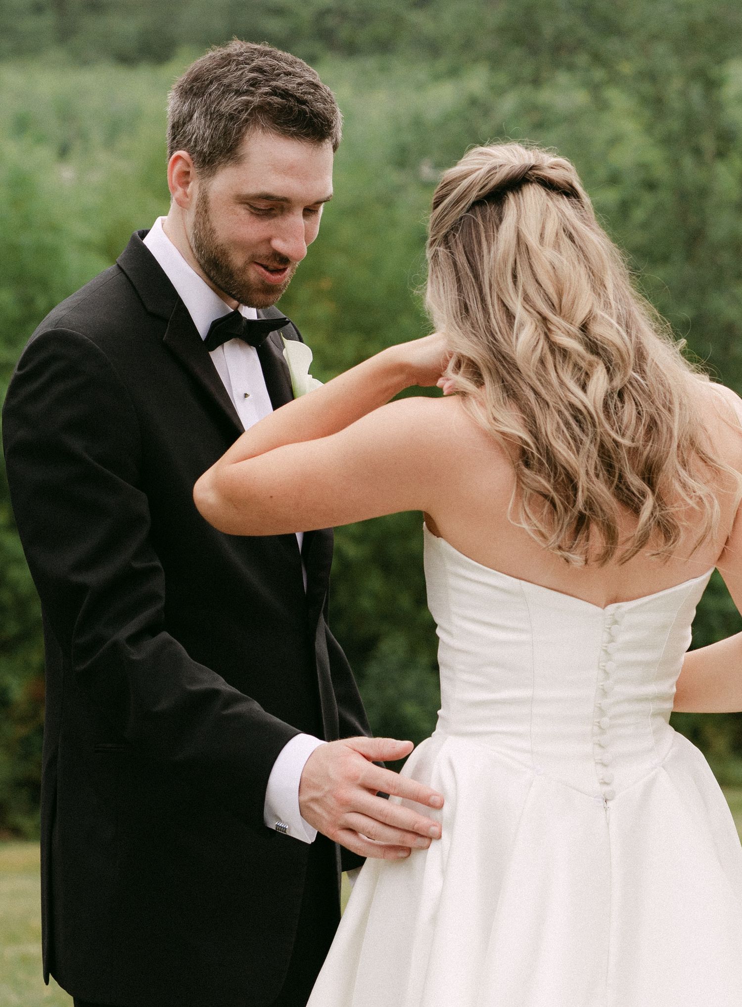 Groom in black tuxedo tenderly holds bride in white strapless gown during outdoor wedding ceremony.