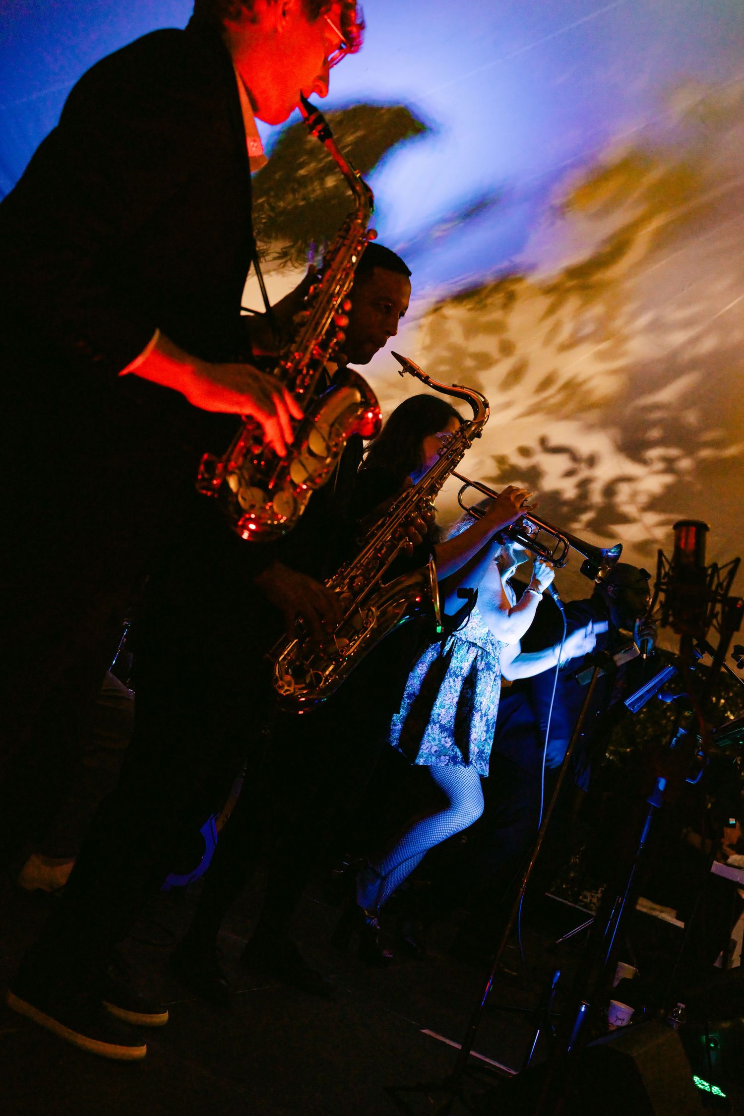 Live band performing at a wedding reception with saxophonists and trumpet player under colorful stage lighting.