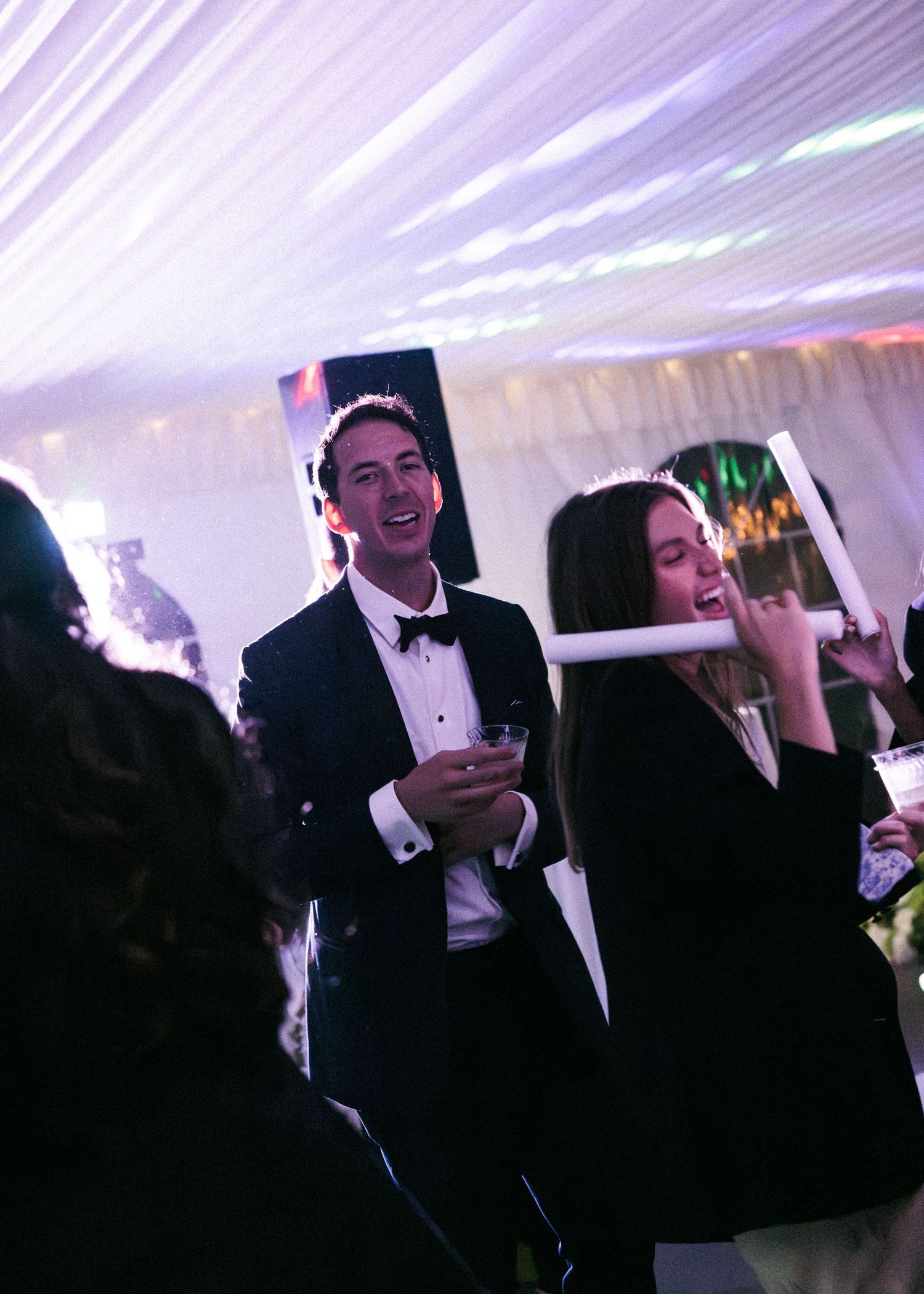 Guests in formal attire celebrate at elegant wedding reception under draped white tent lighting.