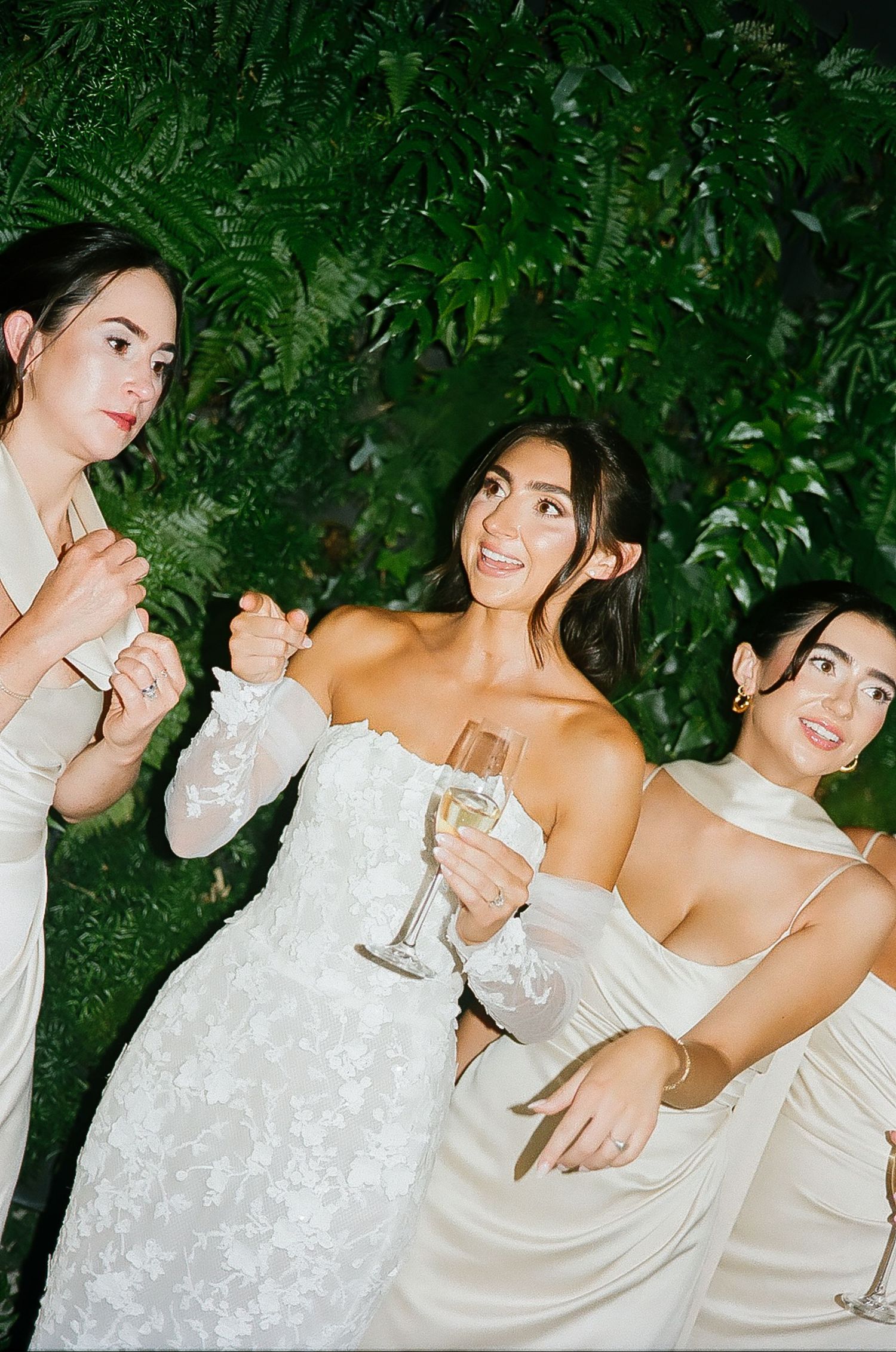 Wedding party in white and champagne dresses poses together against a lush garden backdrop.