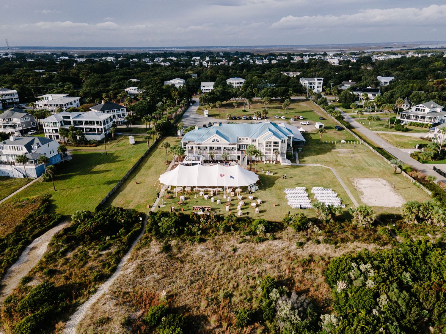Aerial view of coastal wedding venue surrounded by lush greenery with ocean views in background.