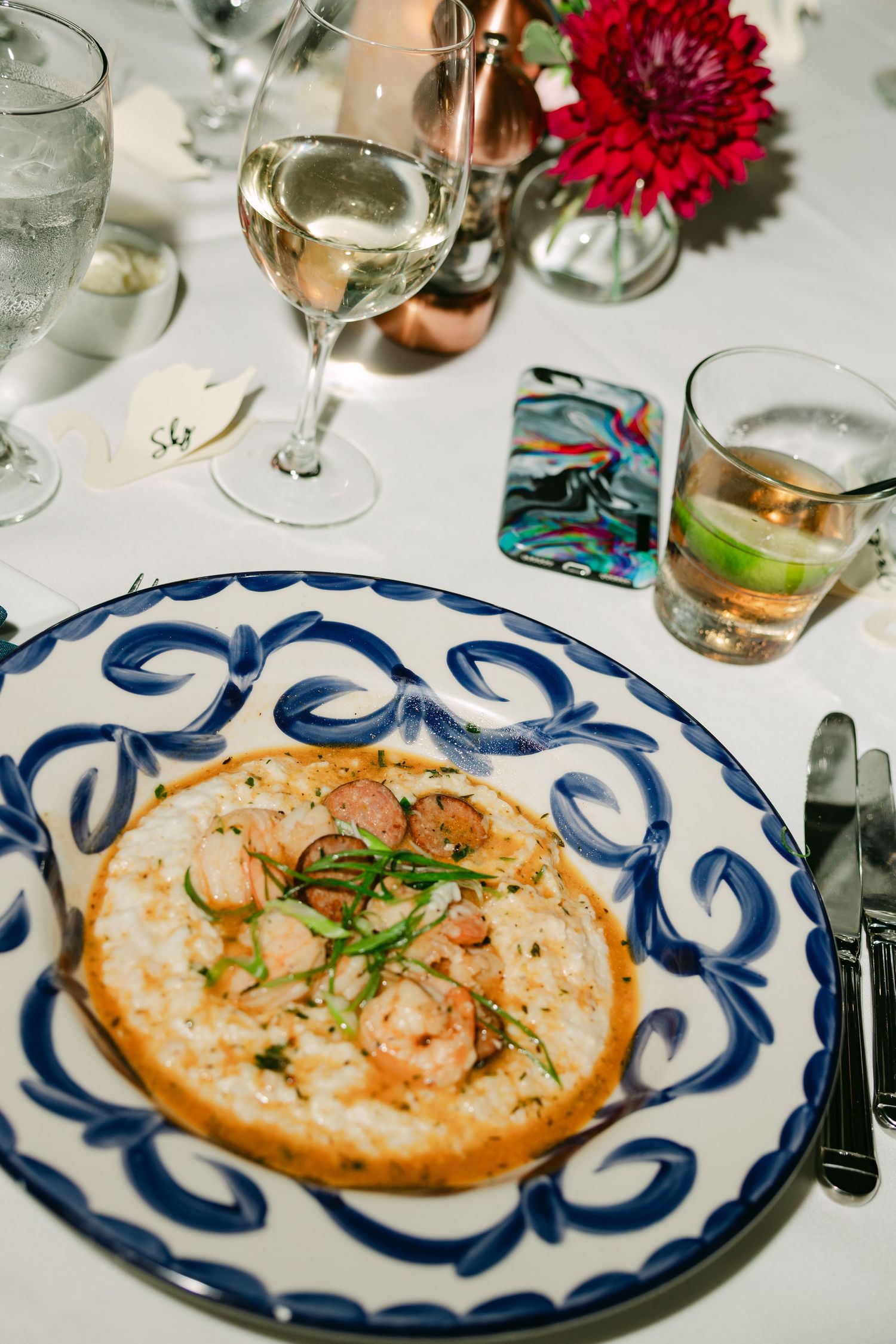 Wedding reception shrimp and grits served on blue and white decorative plate with wine glass.