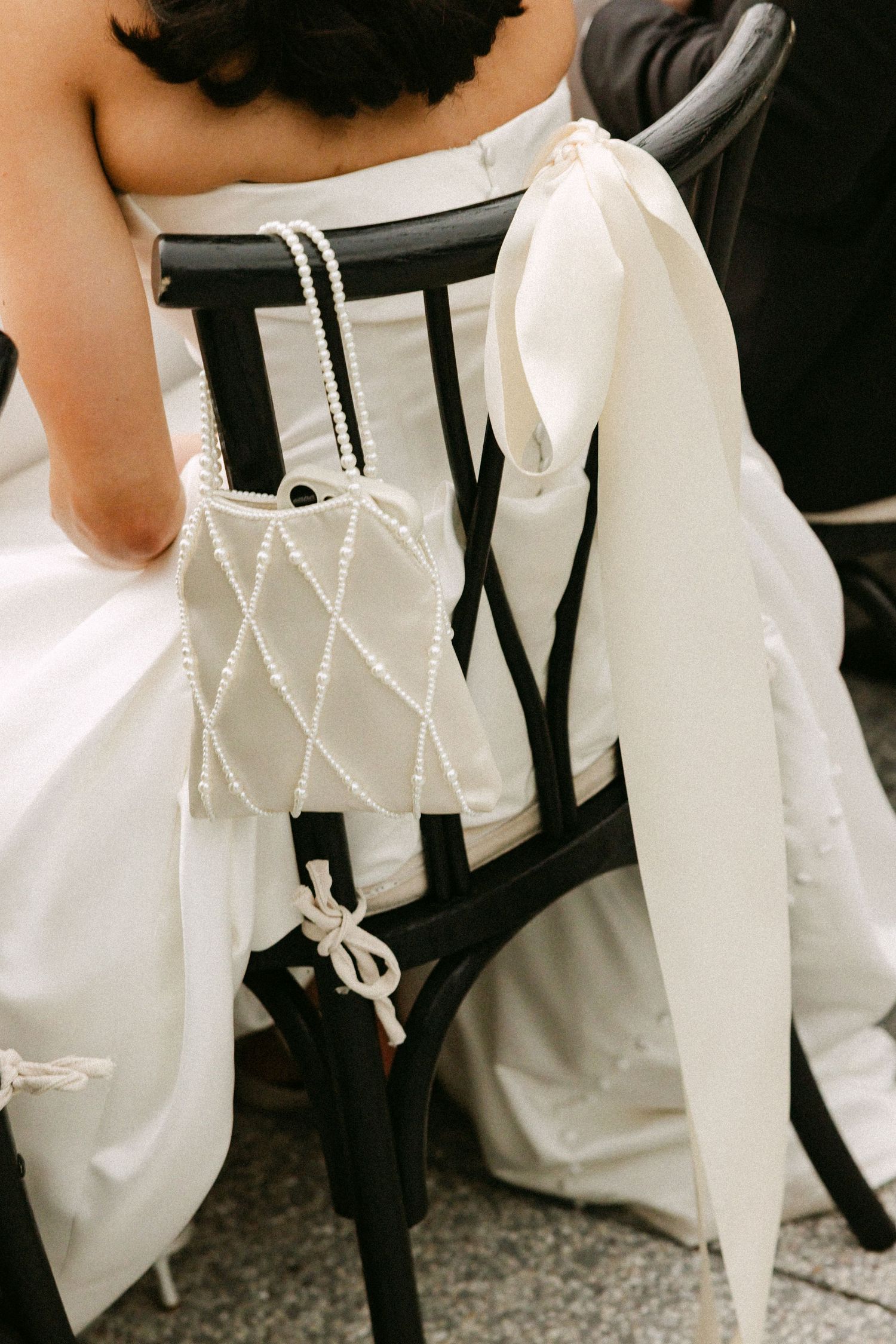 Close-up of bride's pearl quilted handbag and white satin bow on black wedding chair.