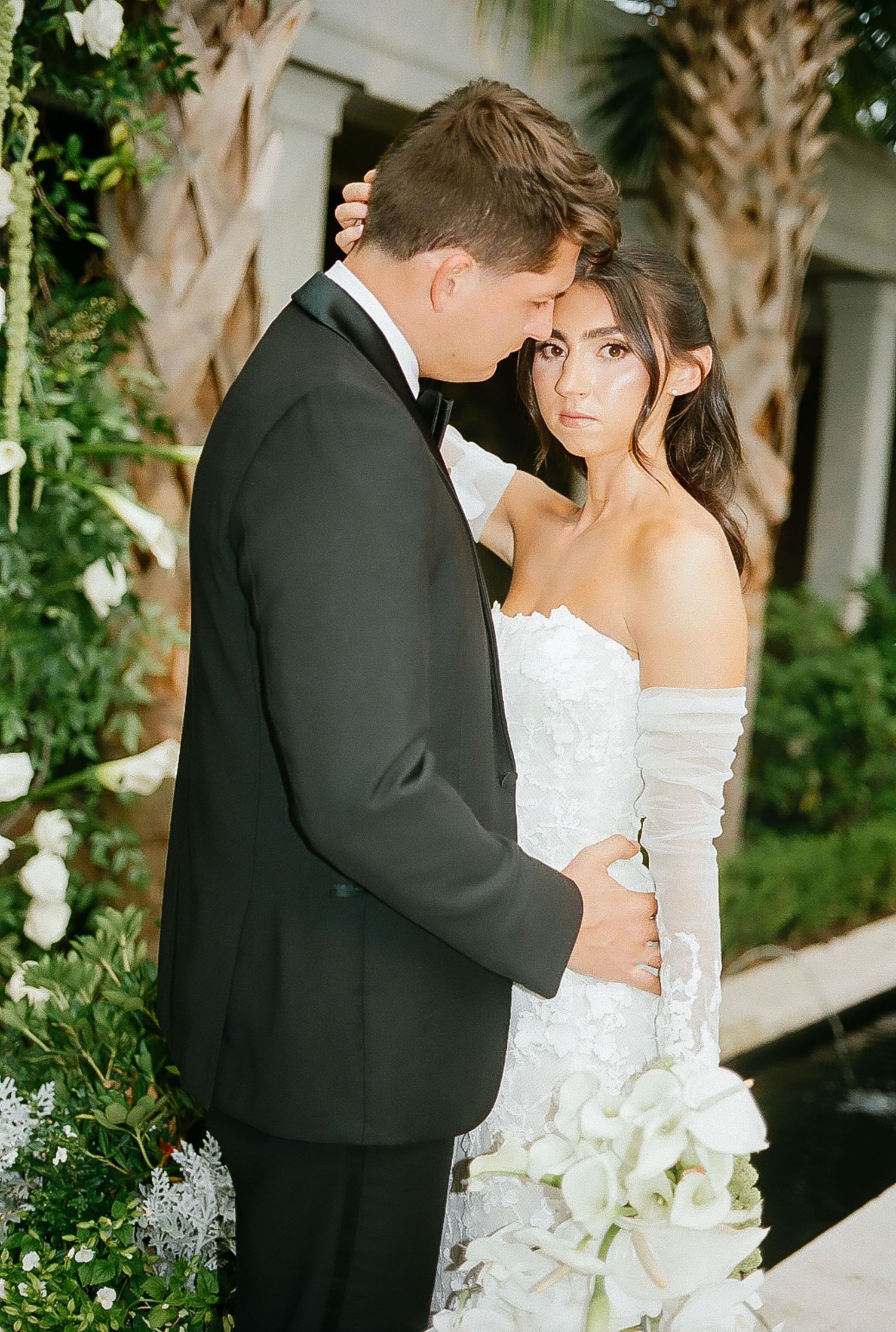 Tender moment between newlyweds surrounded by tropical foliage.