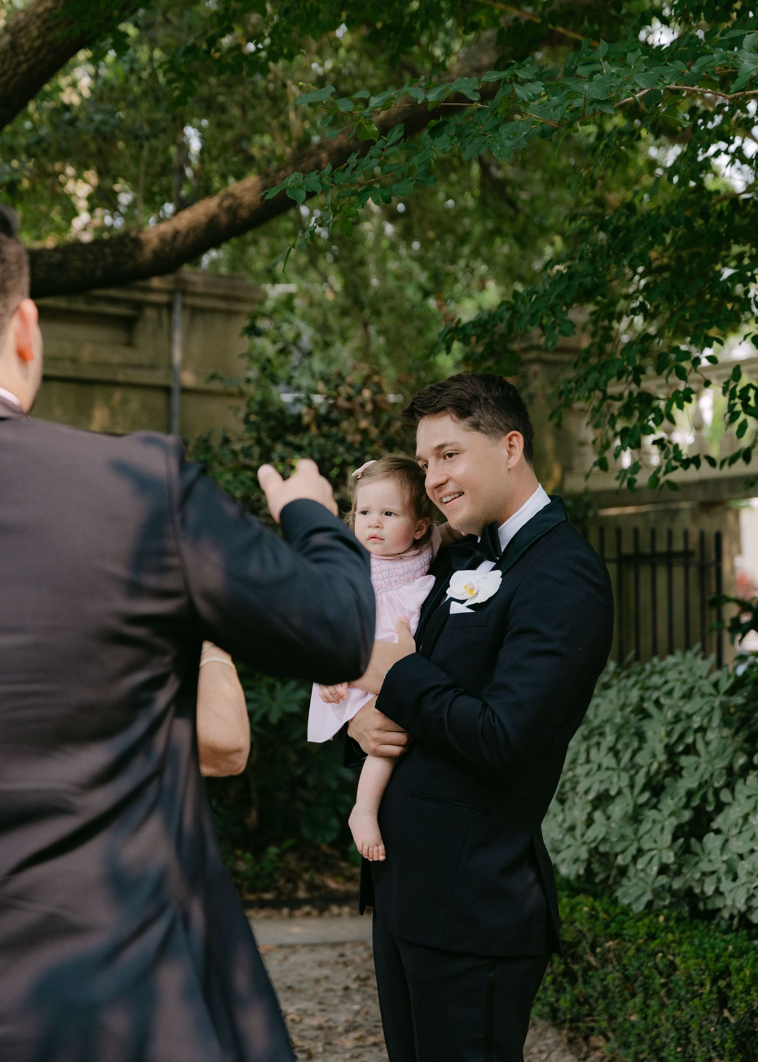 Candid wedding party moments captured outdoors with children in formal wear.