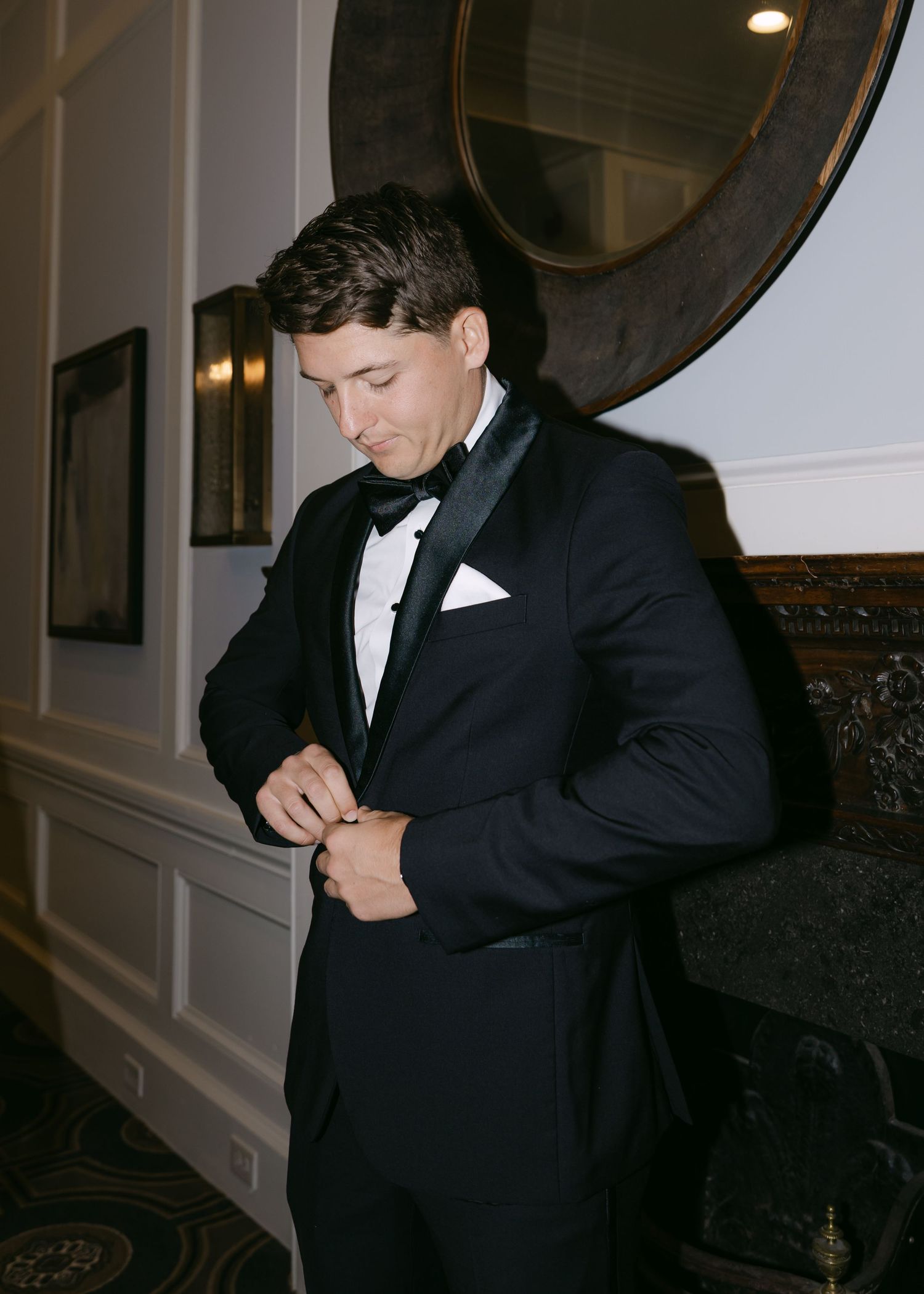 Person adjusting bowtie while wearing classic black tuxedo.