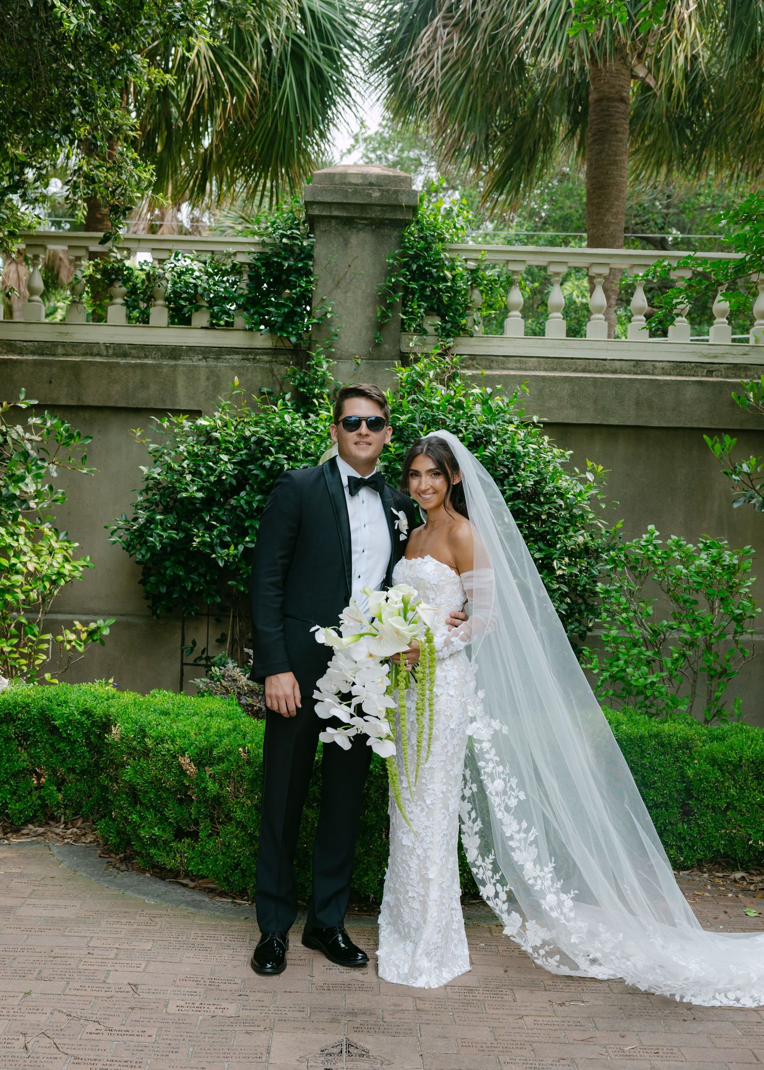 Elegant wedding portraits captured against lush garden backdrop with stone wall details.