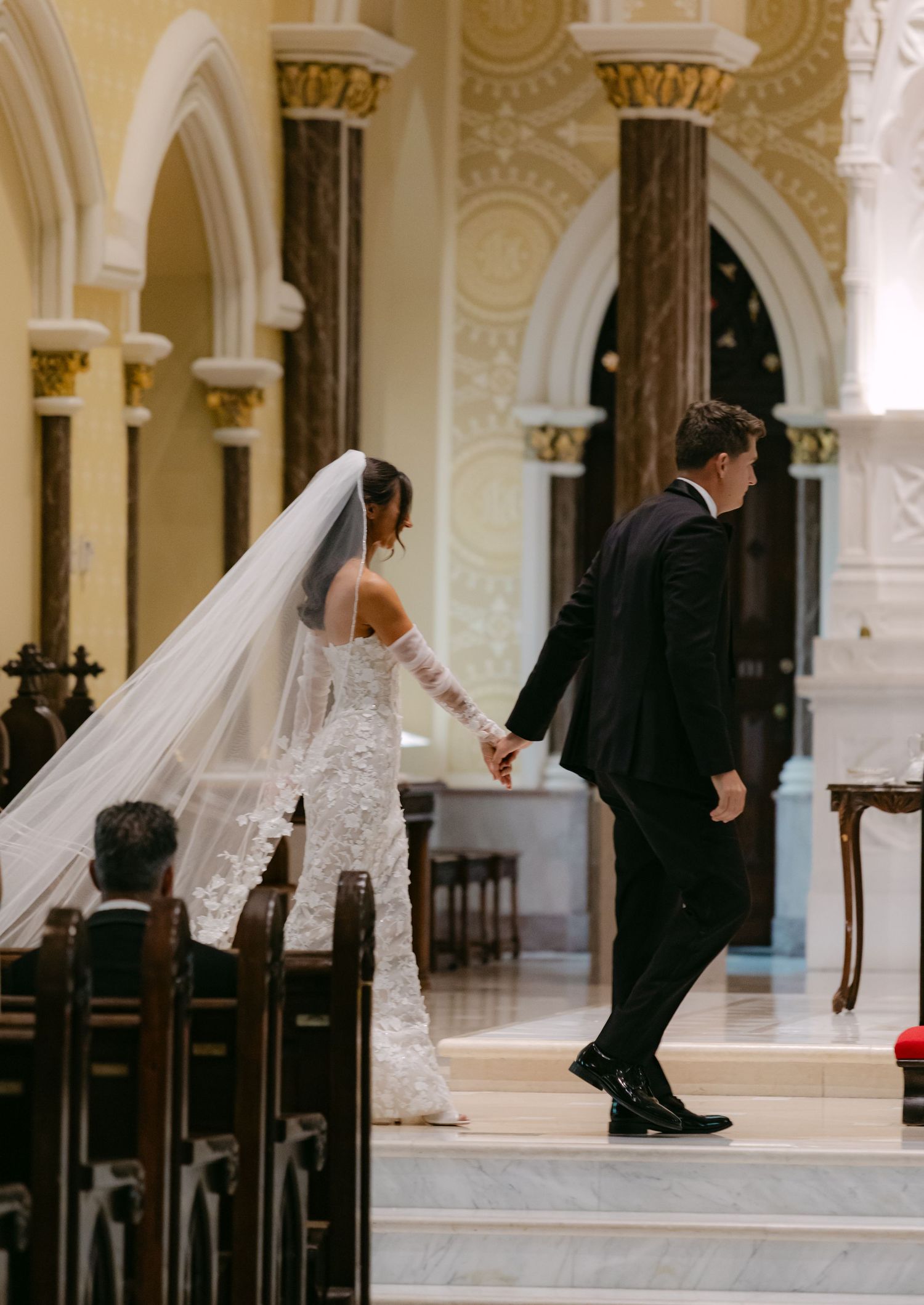 A couple walks down marble steps in a cathedral during their wedding ceremony.