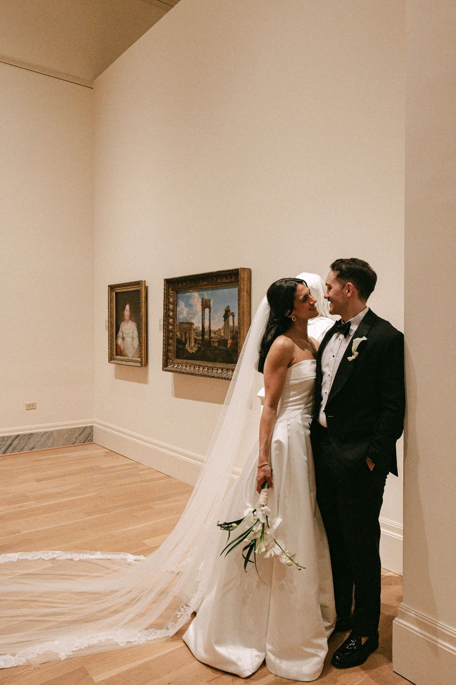 Bride and groom sharing a romantic moment in an art gallery, bride wearing a strapless gown with cathedral veil.