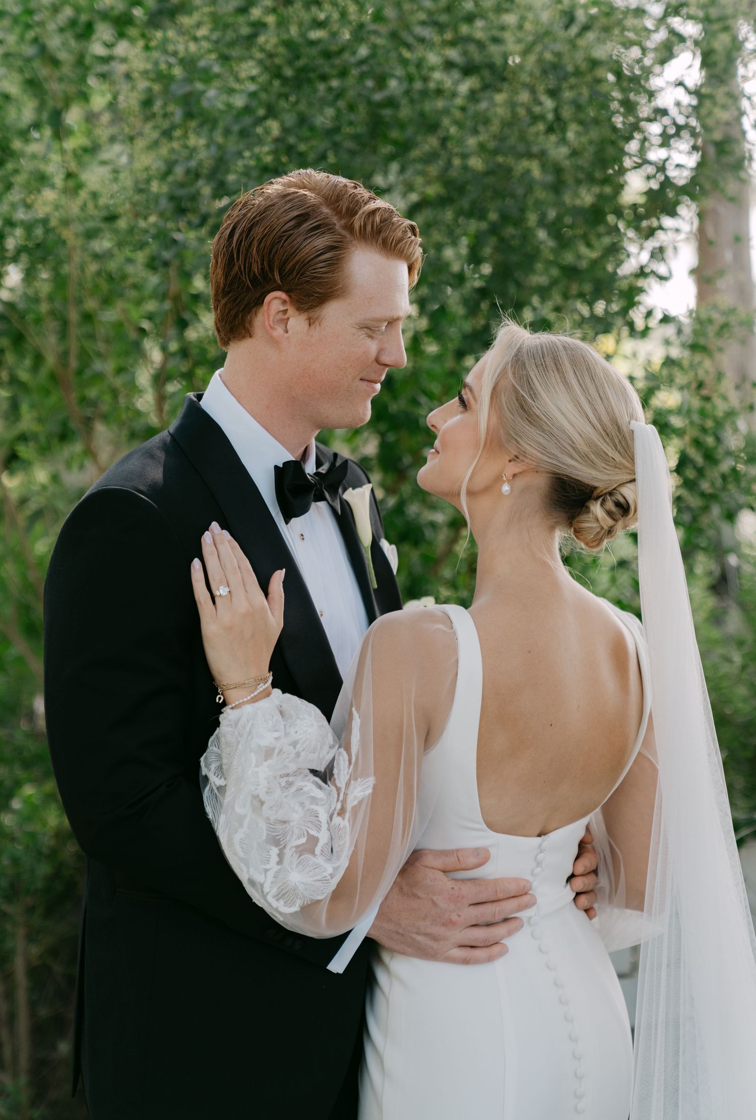 A romantic wedding couple shares intimate moments in a garden setting with flowing white dress and black tuxedo.