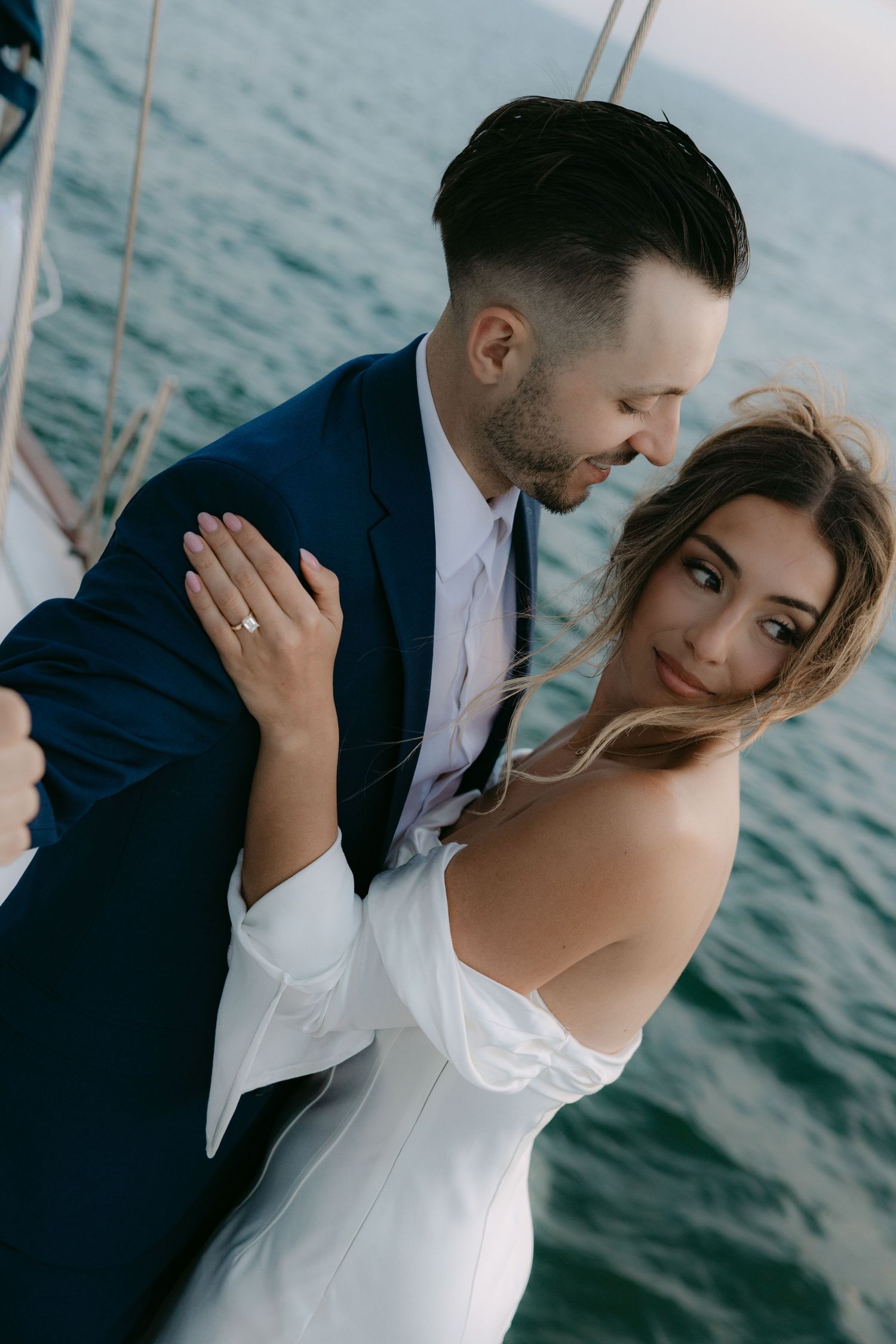 A couple shares an intimate moment on a boat against a serene ocean backdrop.
