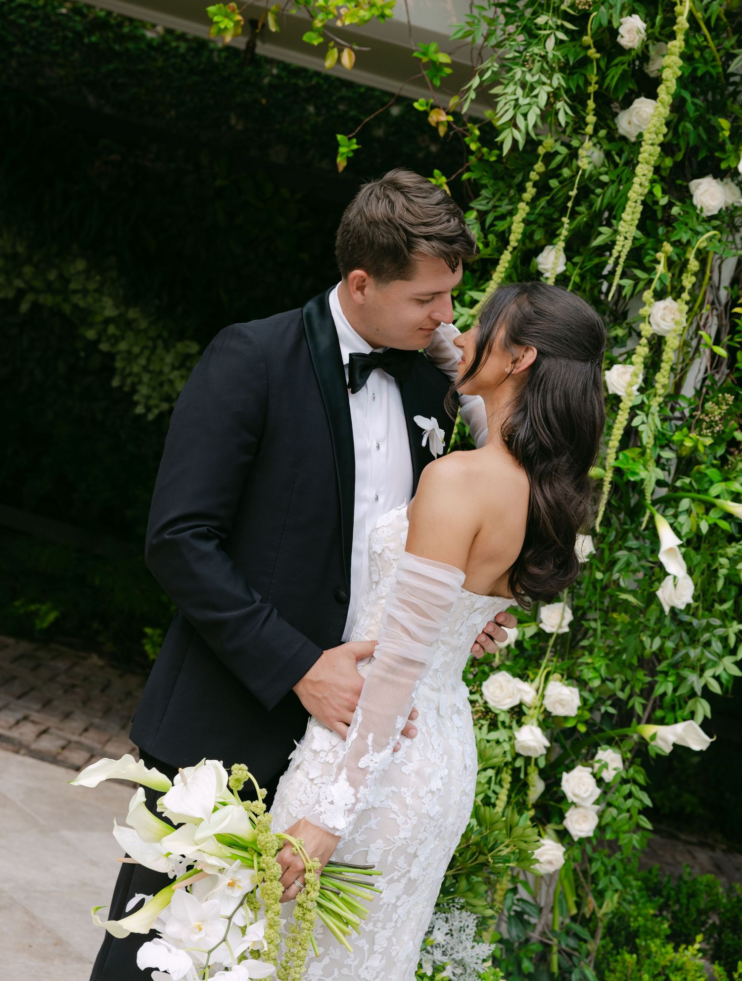 Intimate garden wedding moment with couple surrounded by white flowers and climbing vines.
