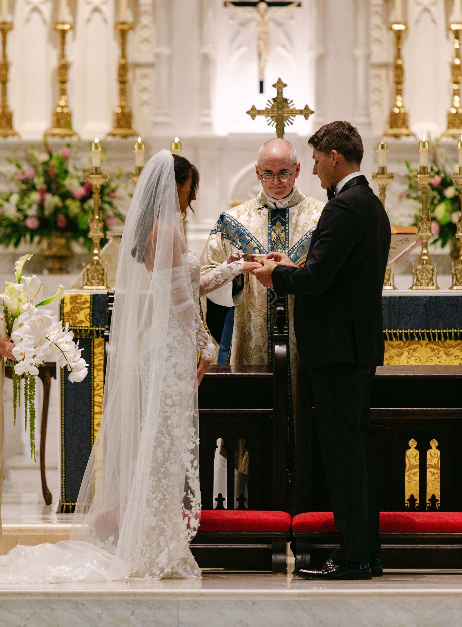 A wedding ceremony being performed by a priest at an ornate church altar with golden decorations.
