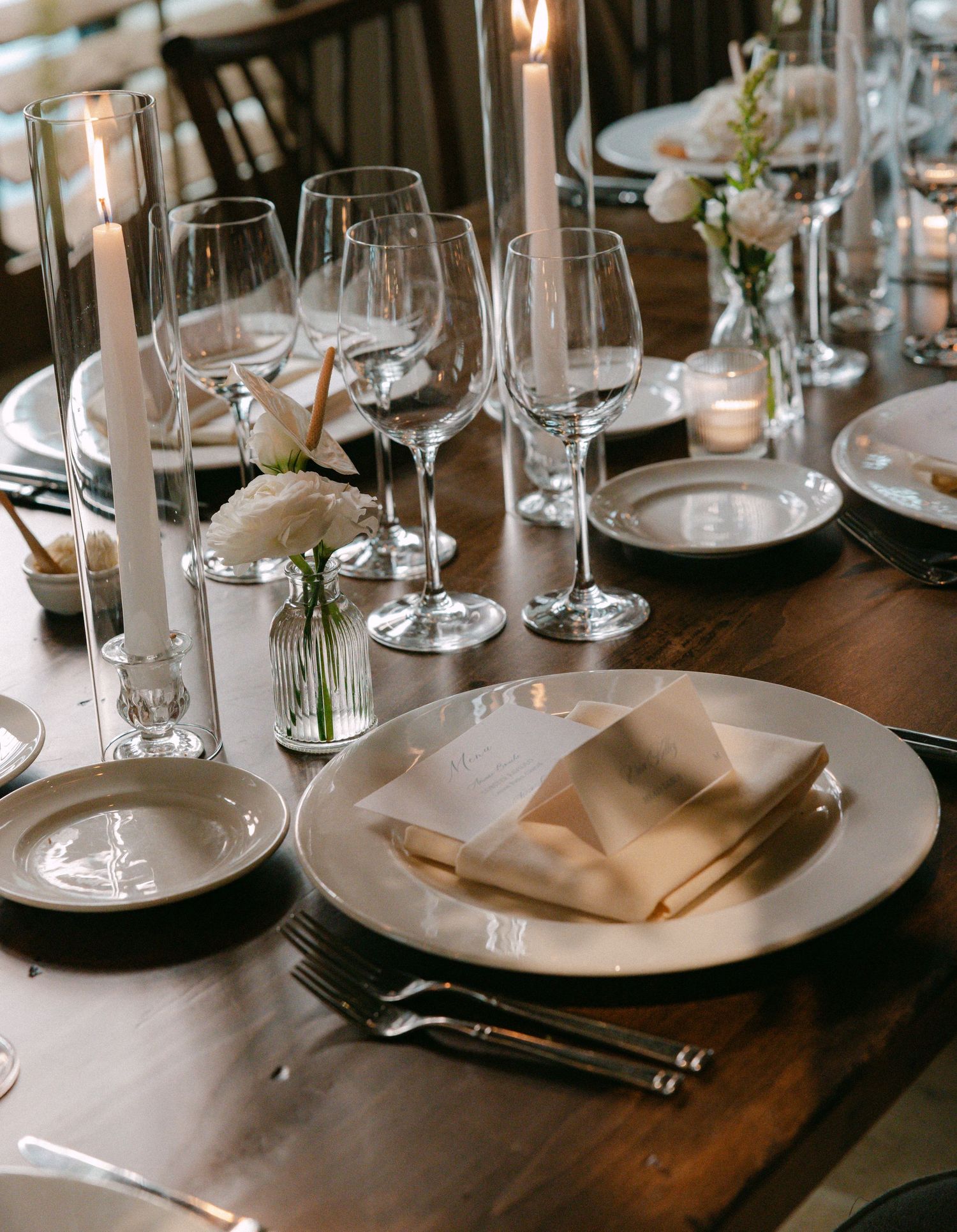 Close-up of formal place settings with beige napkins and wine glasses on dark wooden tables.