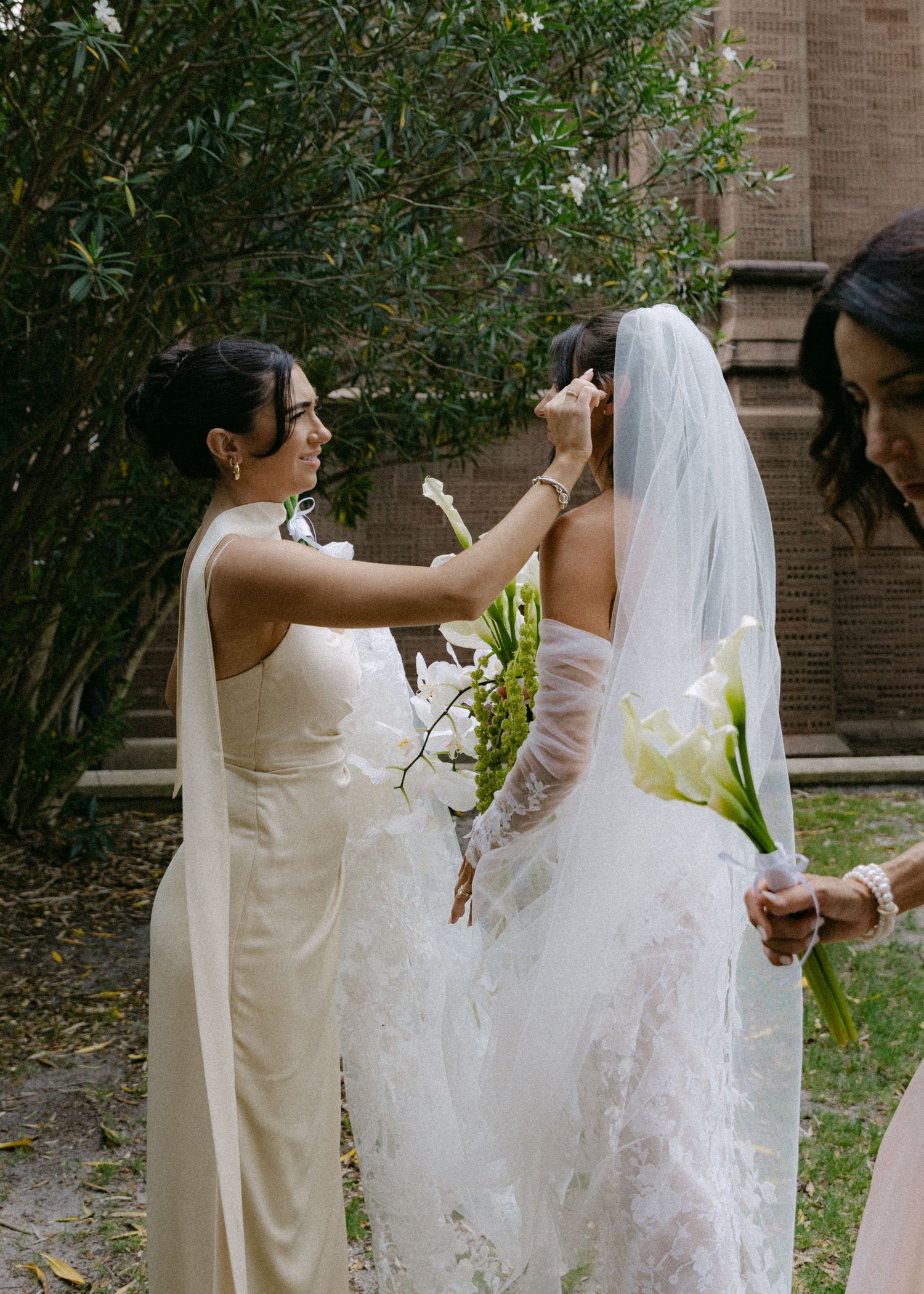 Bridal party members helping adjust the train of an elaborate white wedding gown.