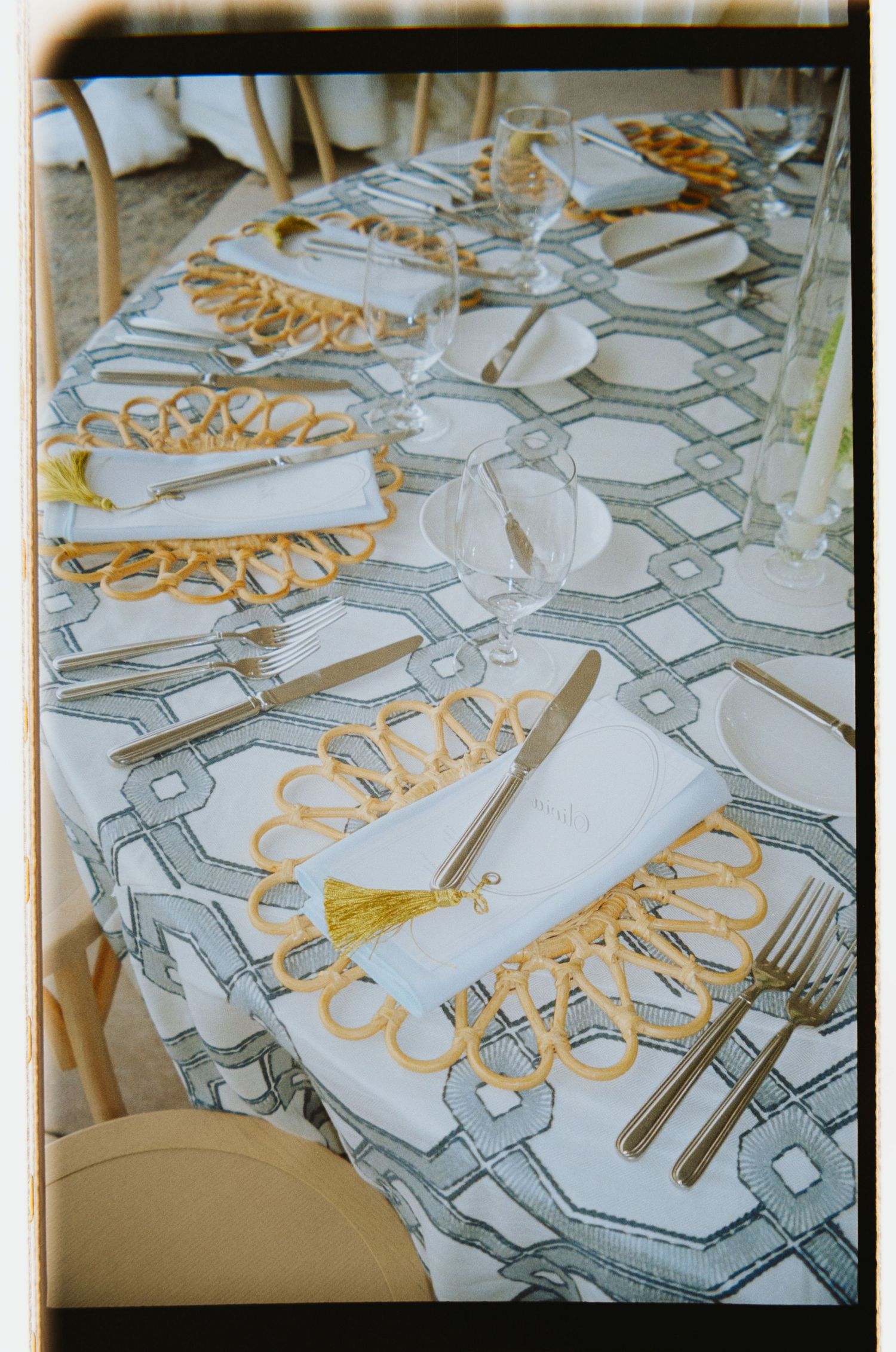 Elegant table setting with gold napkin rings, geometric patterned tablecloth, crystal glasses, and gold cutlery for a formal event.