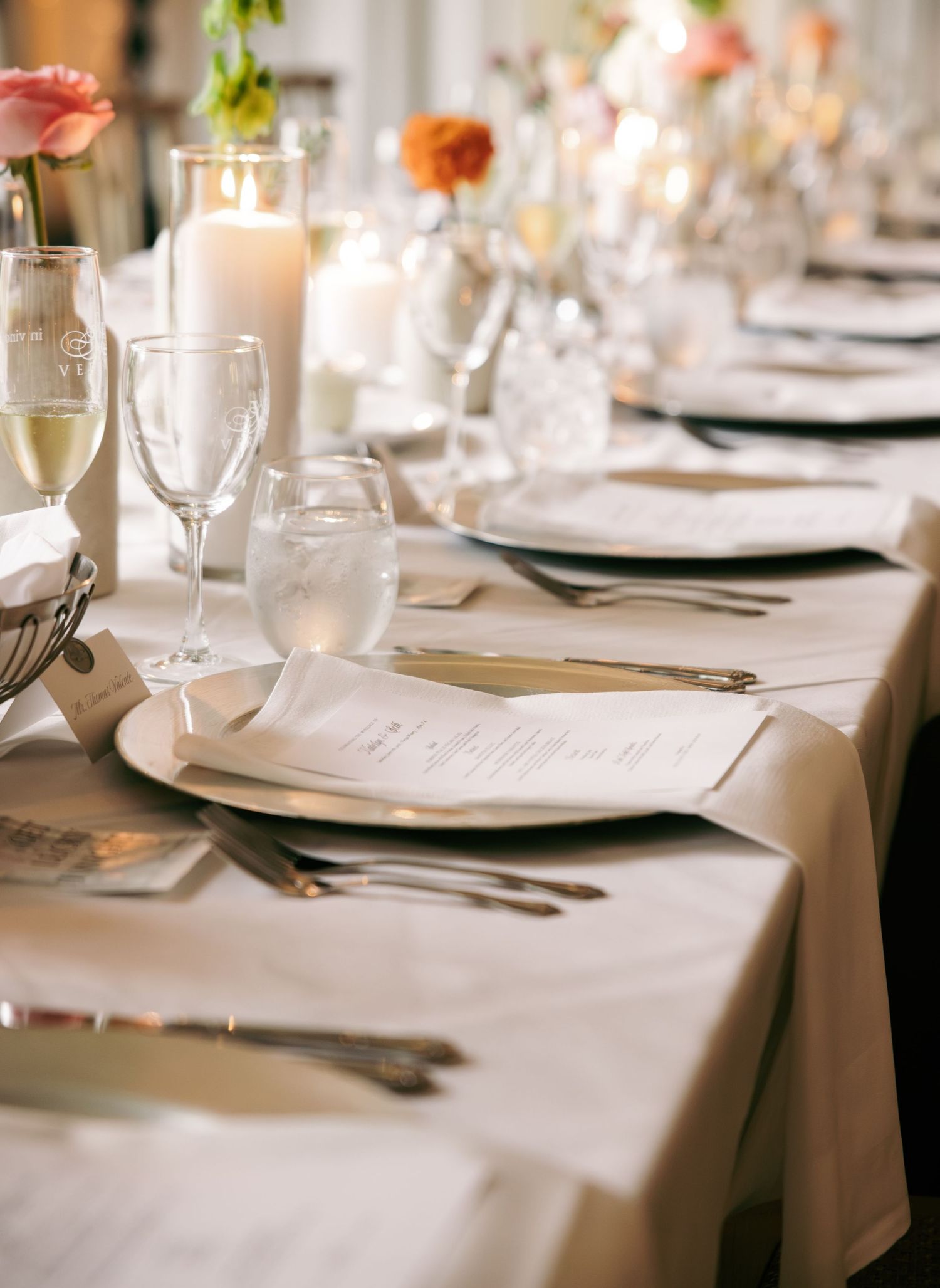 Elegant wedding reception table setting with white linens, crystal glassware, candles, and neatly folded menu cards.