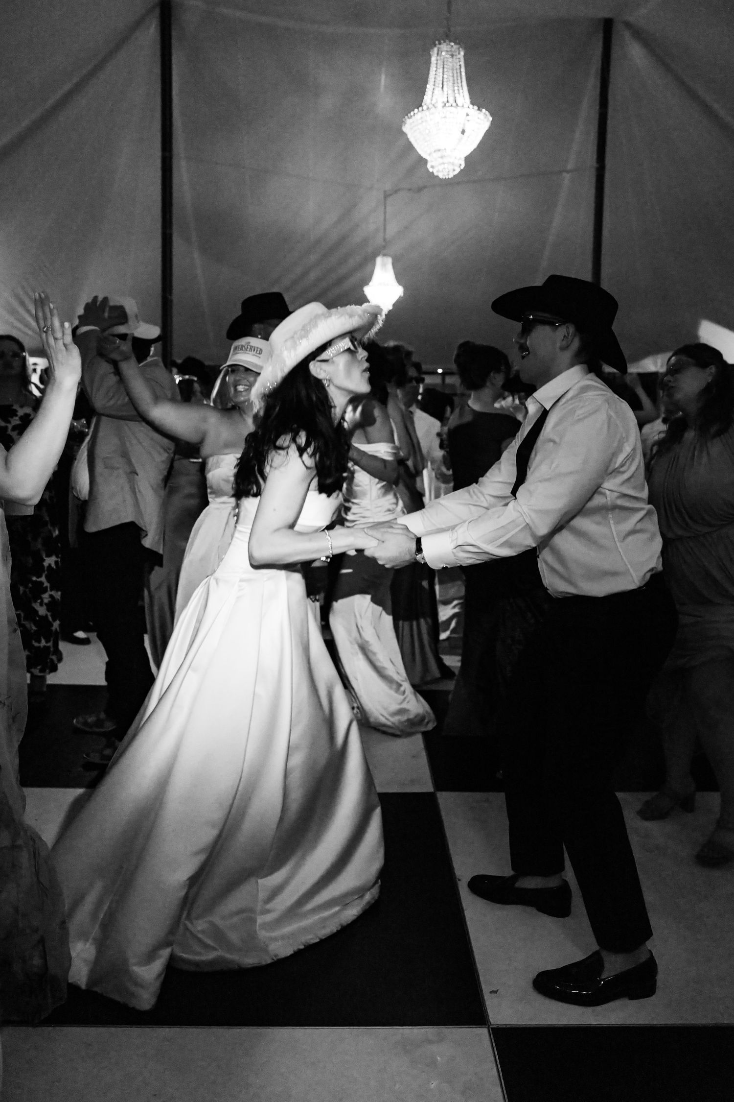Bride and groom dance in cowboy hats on checkered dance floor at wedding reception.