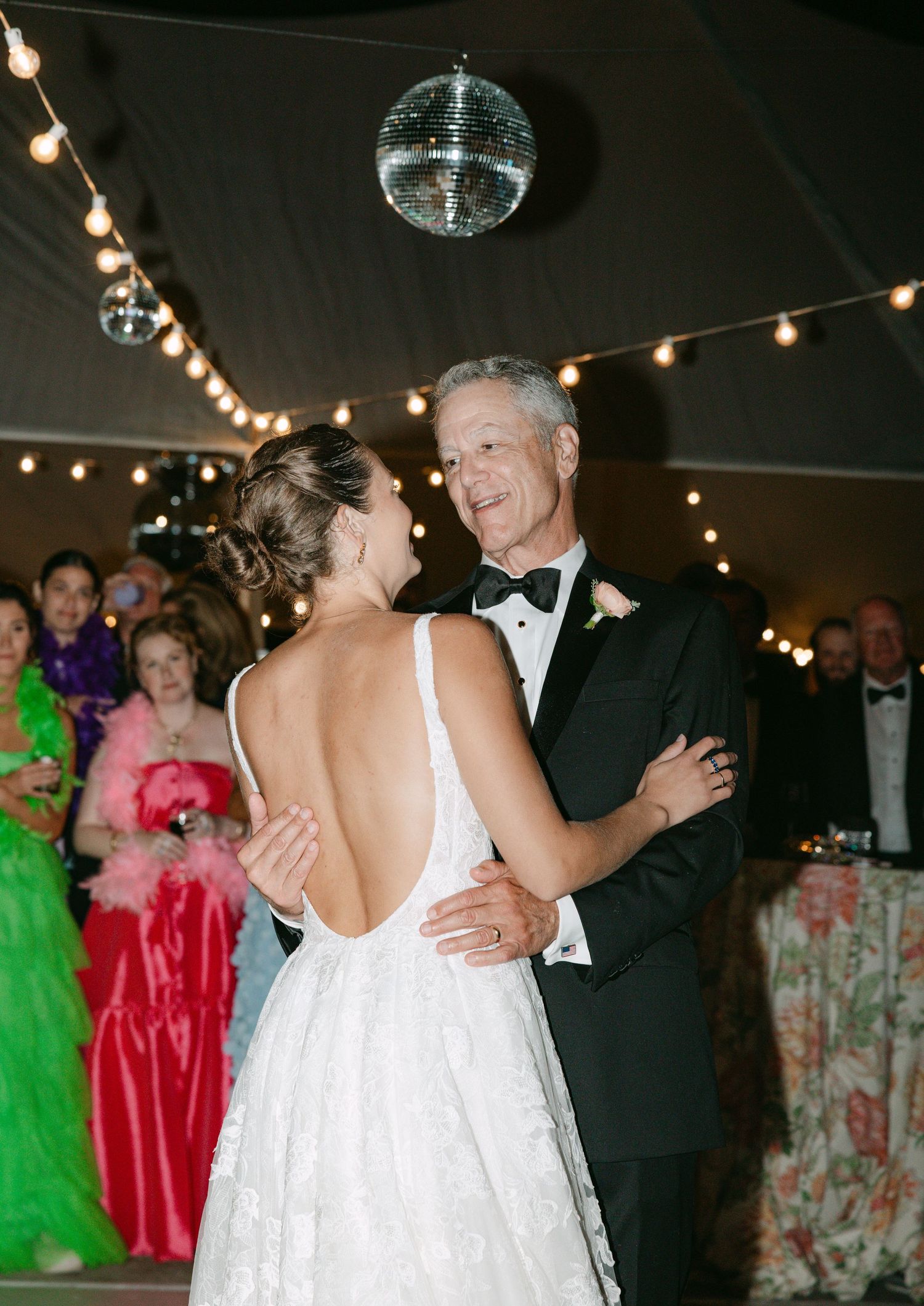 Bride and groom sharing first dance under disco ball in elegant wedding tent.