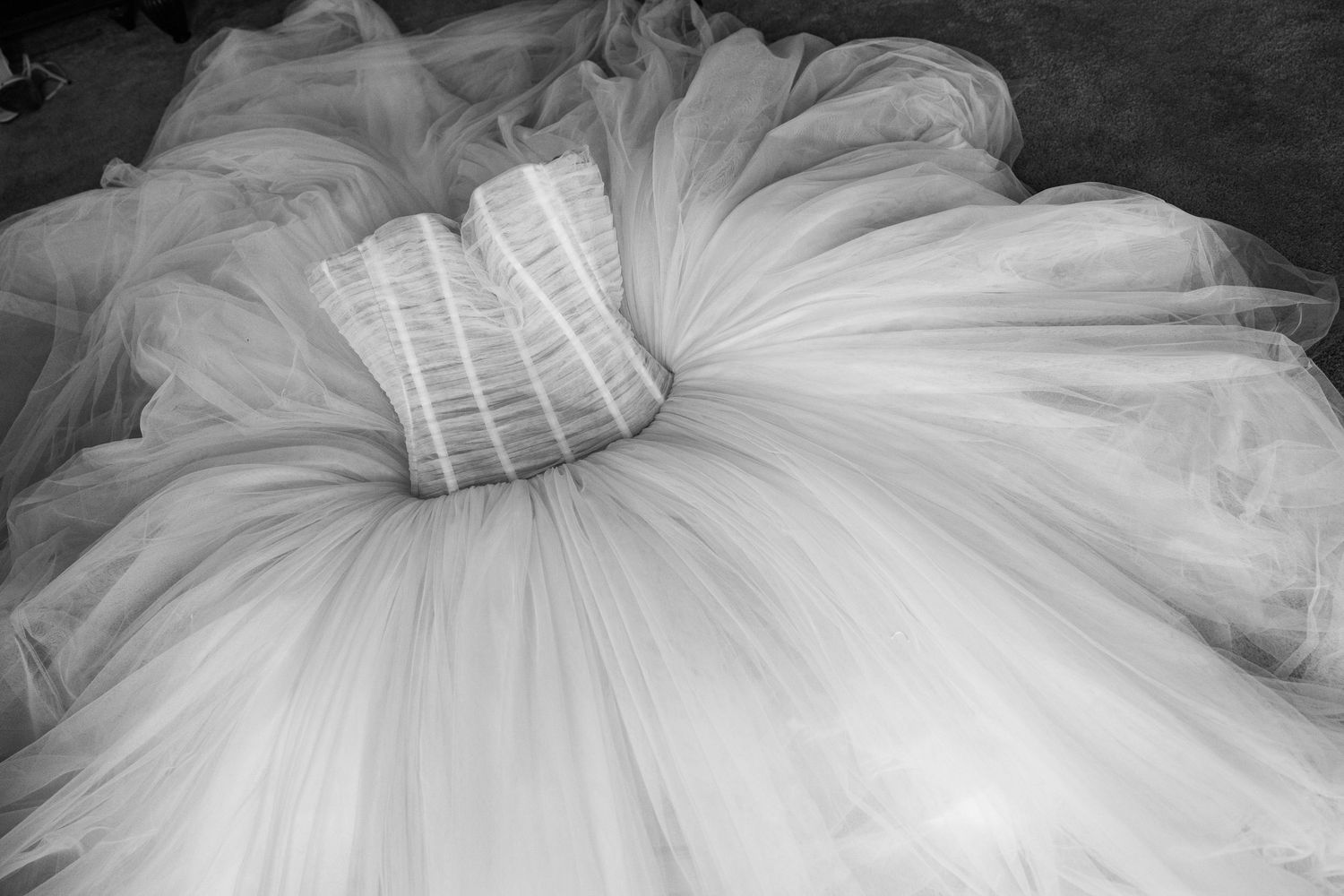 Black and white photo of an elegant wedding dress with a full tulle skirt and structured corset bodice spread on the floor.