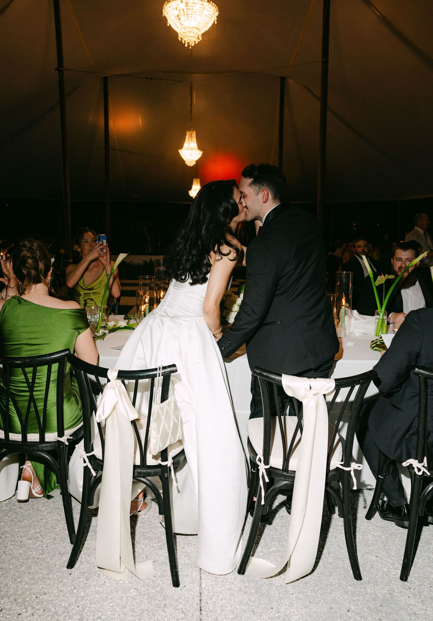 Bride and groom share intimate moment at sweetheart table during elegant tented wedding reception at night.