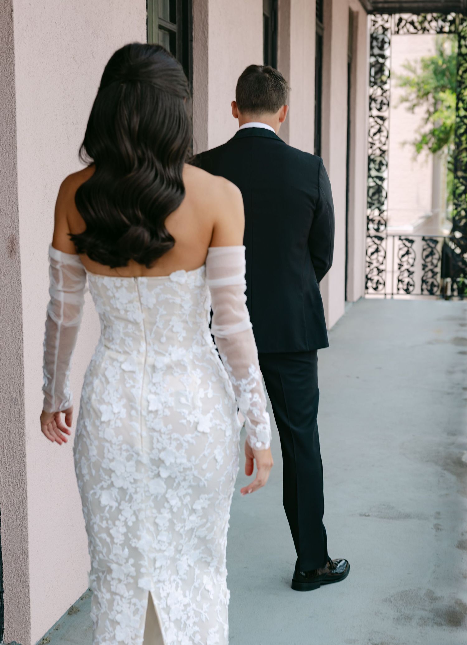 A couple in wedding attire walking down an elegant covered walkway with columns.