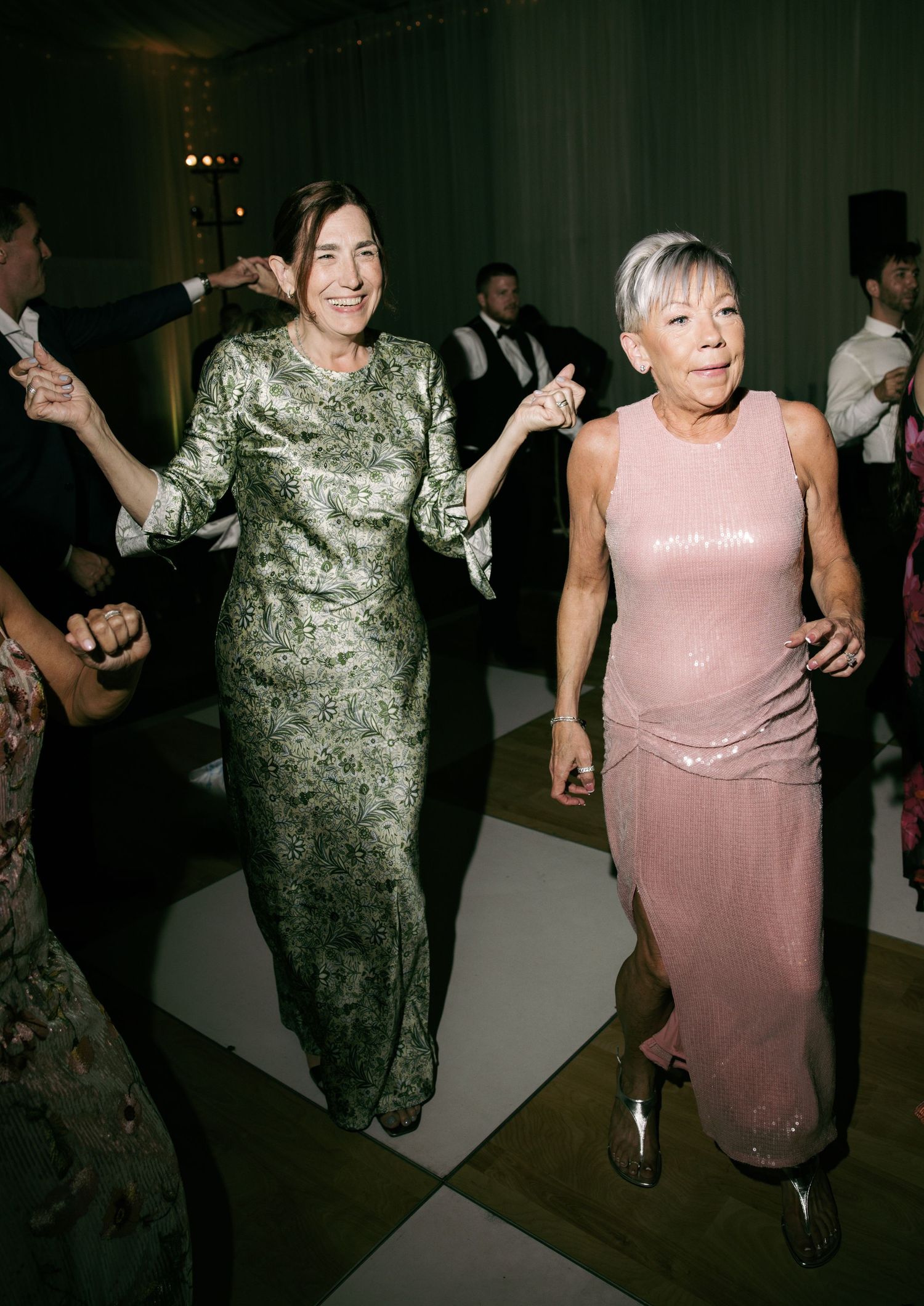 Two women in elegant gowns dancing joyfully at a wedding reception celebration.