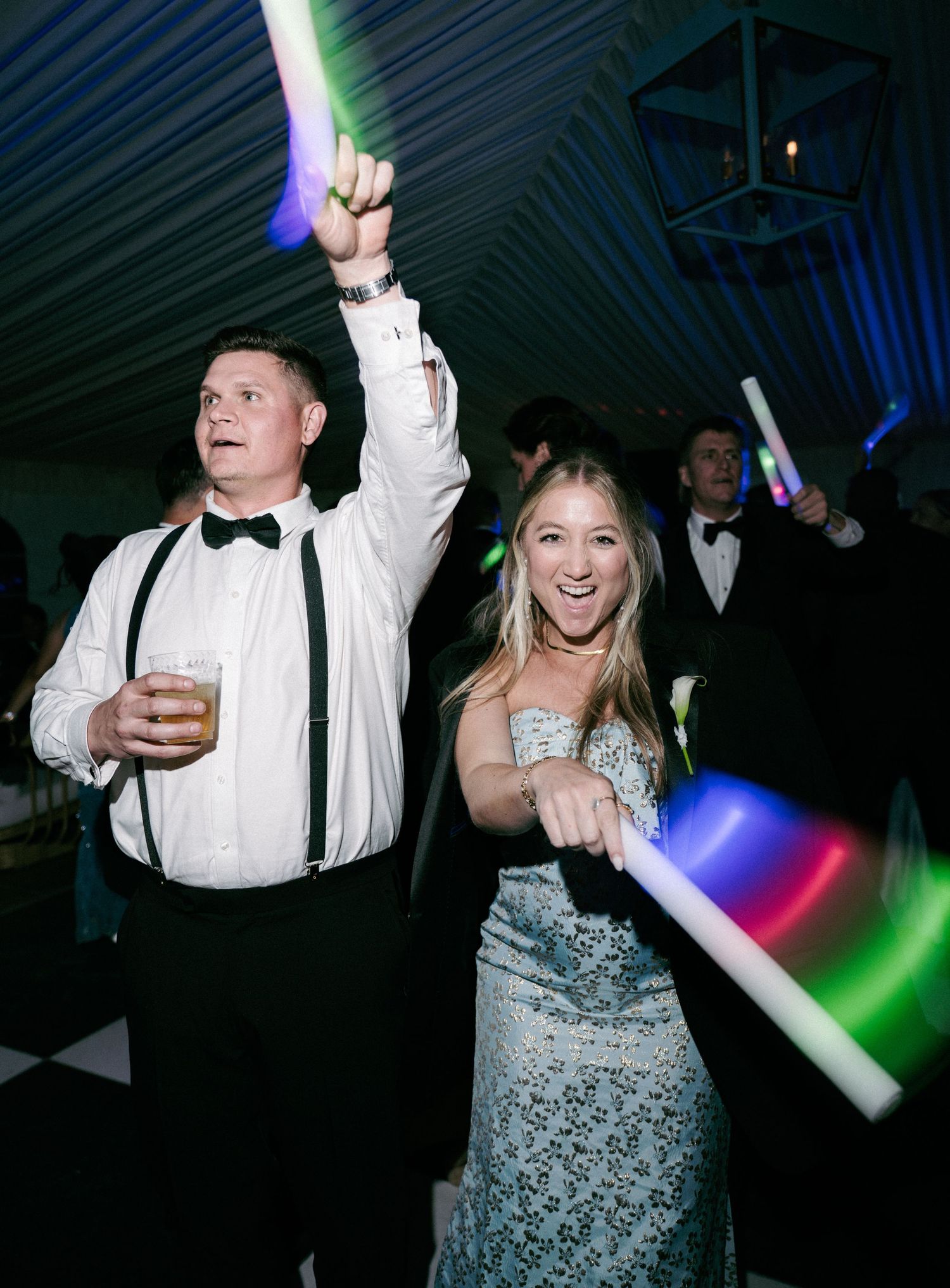 Couple dancing at wedding reception with glowing LED wands and colorful lights under a tent.