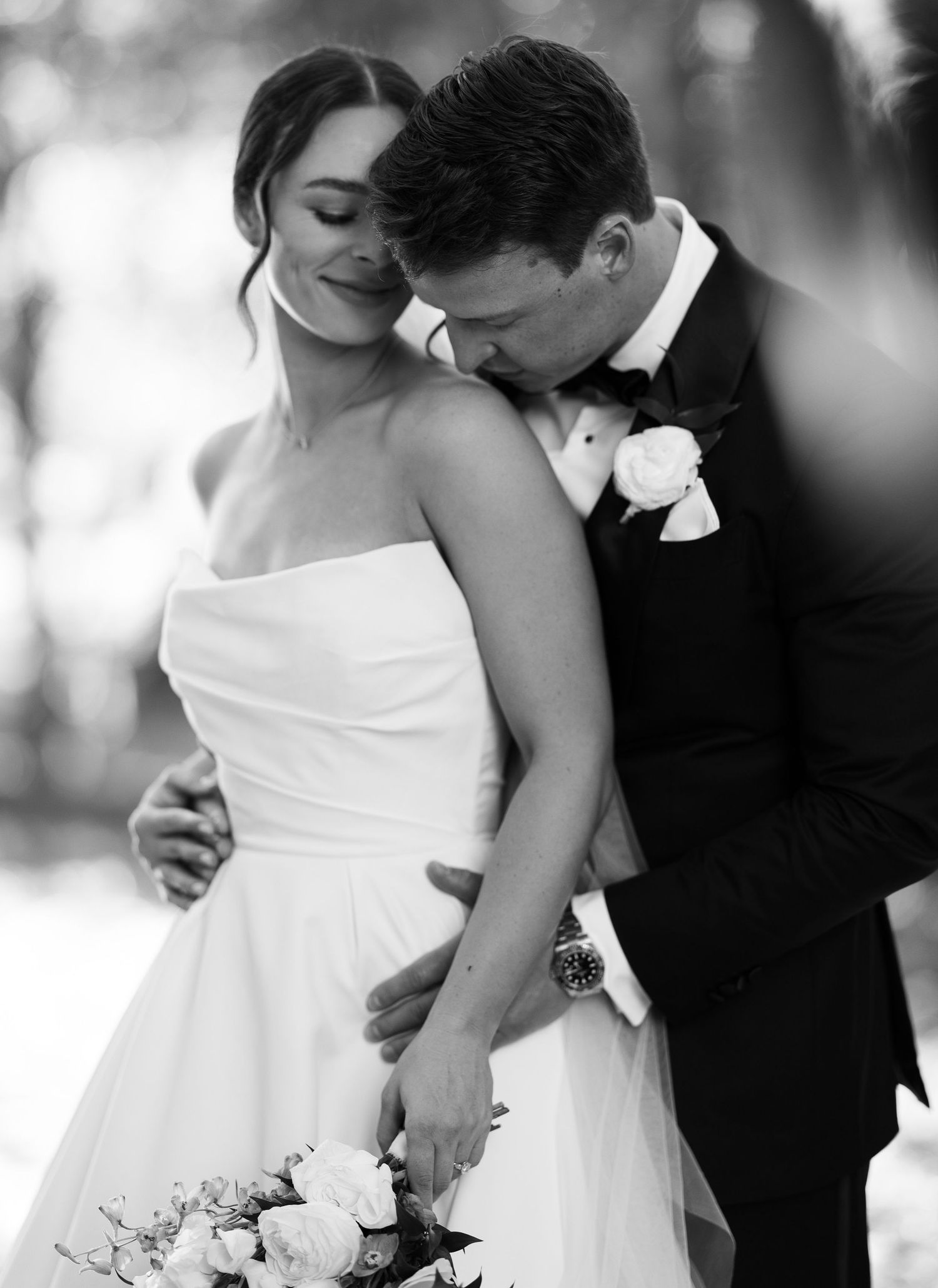 Black and white wedding photo of bride in strapless gown and groom in tuxedo sharing a tender embrace.