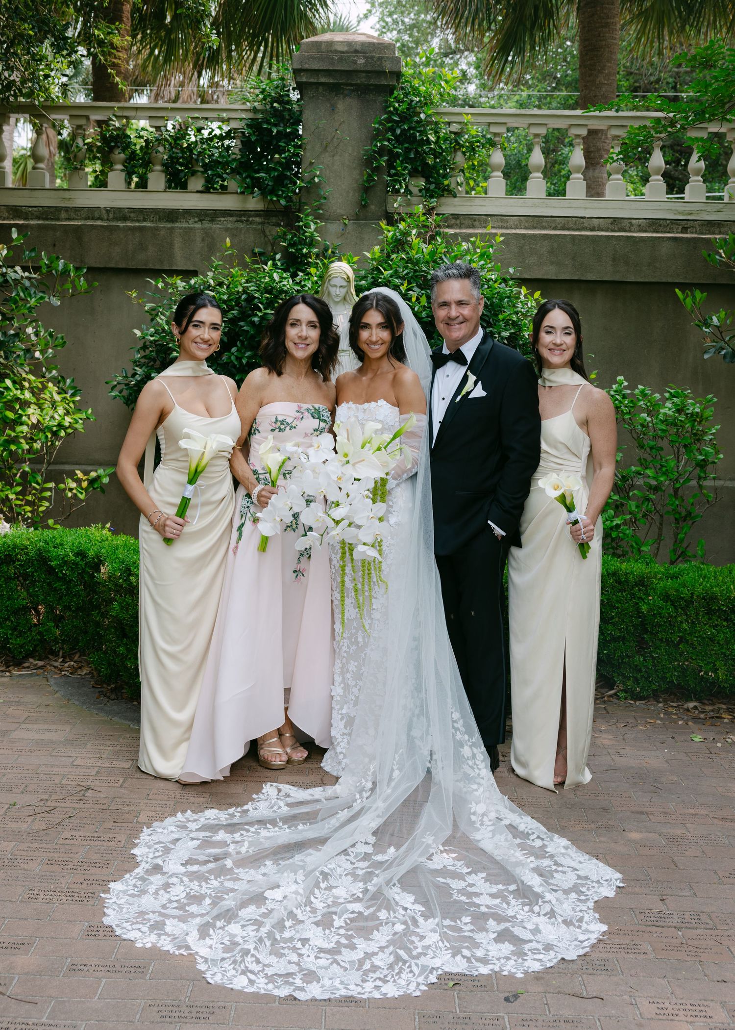 Beautiful wedding party gathered outdoors with bridesmaids in cream dresses and flowing white gown.
