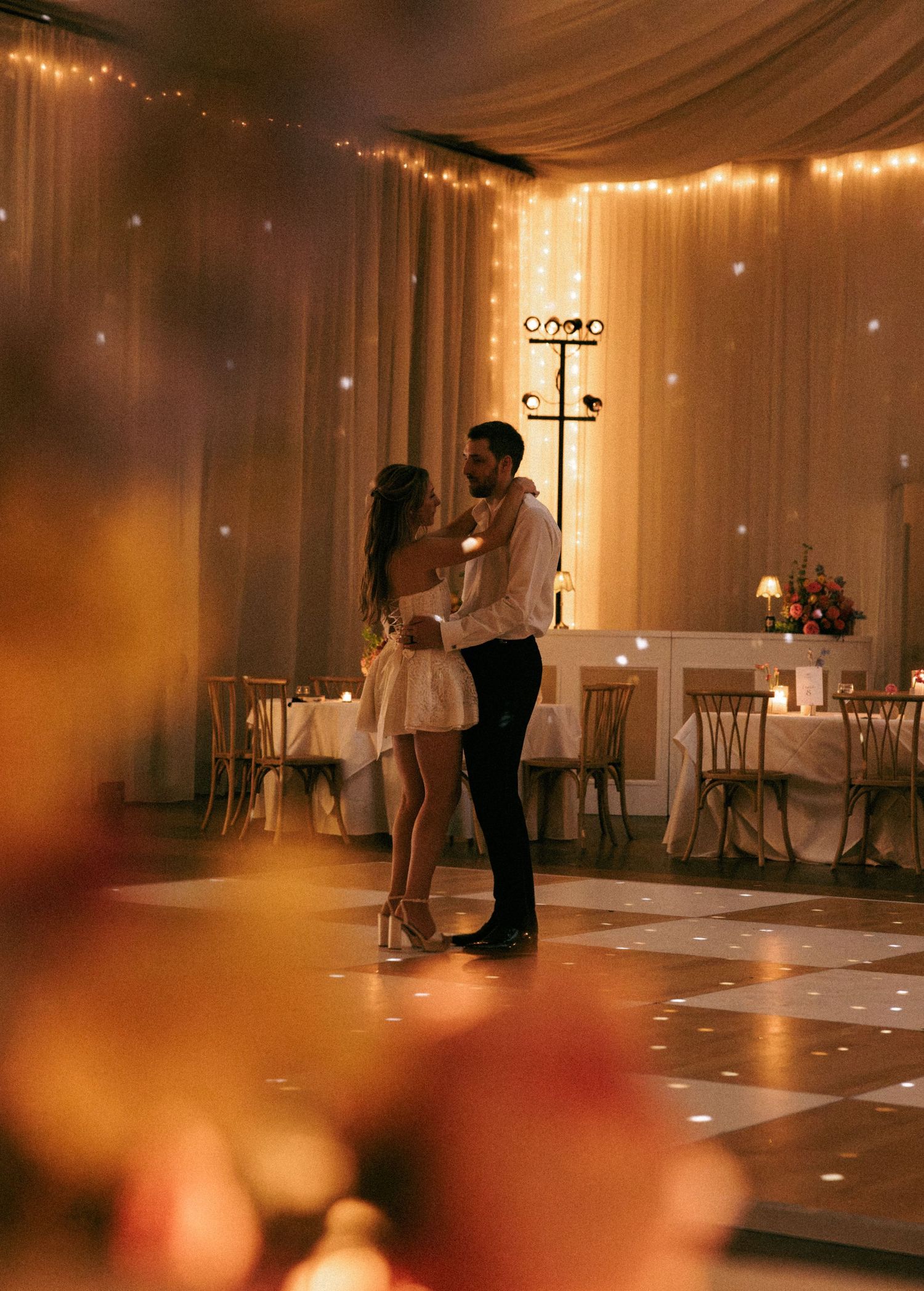 Couple sharing their first dance at a romantic wedding reception with warm fairy lights and elegant draping.