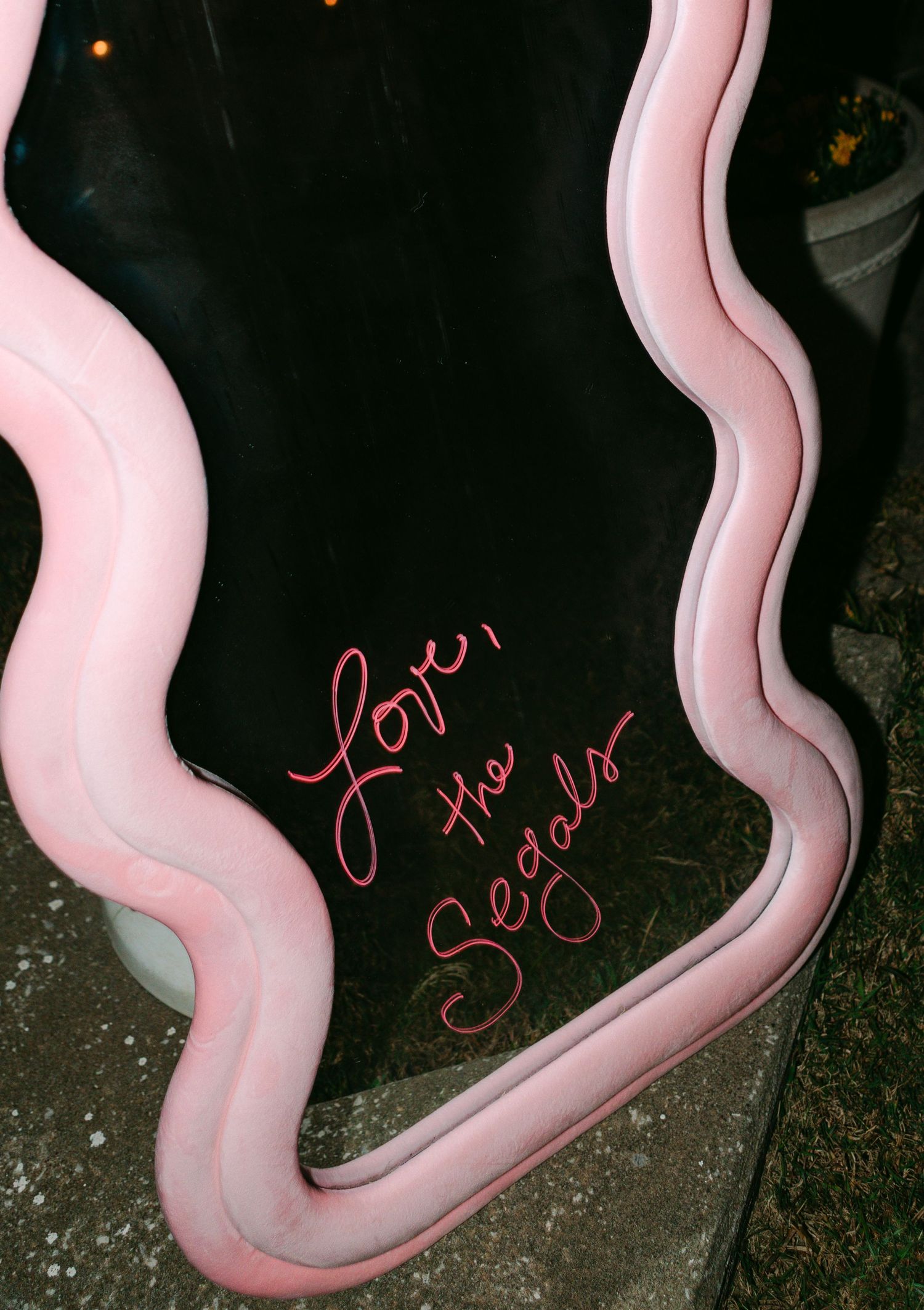 Decorative wavy pink mirror sign reading Love the Segals at an outdoor wedding reception at night.