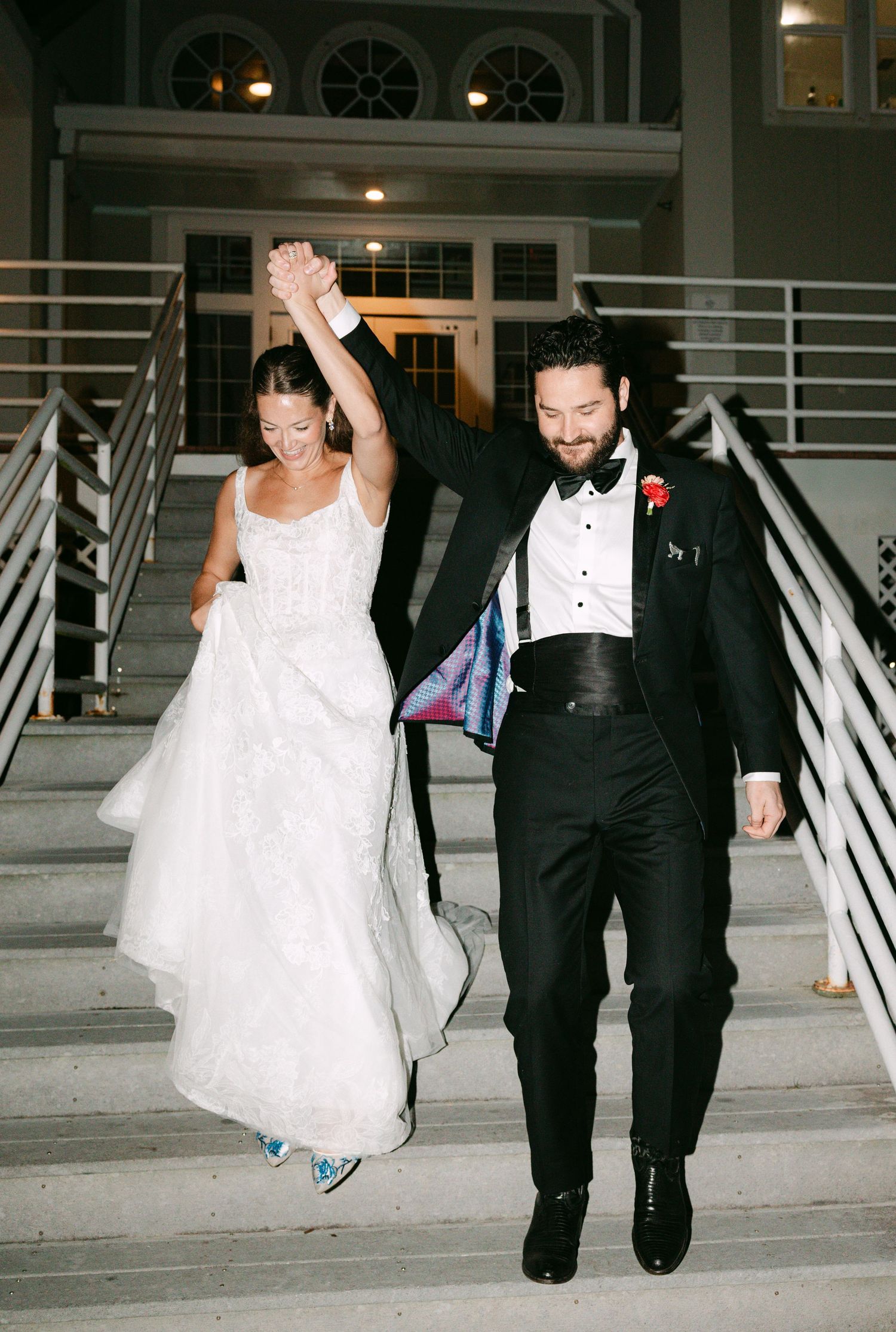 Bride and groom celebrating on staircase, raising hands triumphantly after their wedding ceremony.