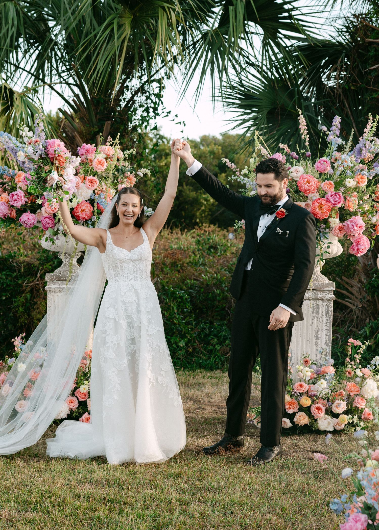 Bride and groom celebrate at outdoor wedding ceremony surrounded by colorful floral arrangements and palm trees.