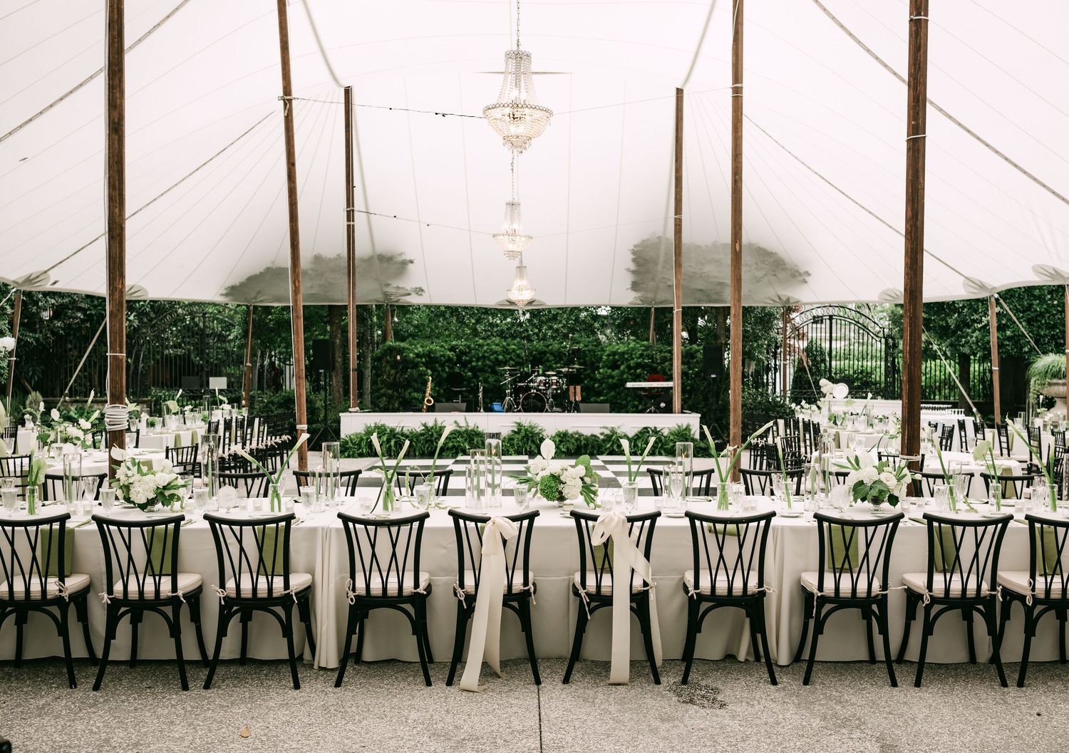 Elegant wedding reception under a sailcloth tent with long tables, white linens, greenery centerpieces, and black chiavari chairs.